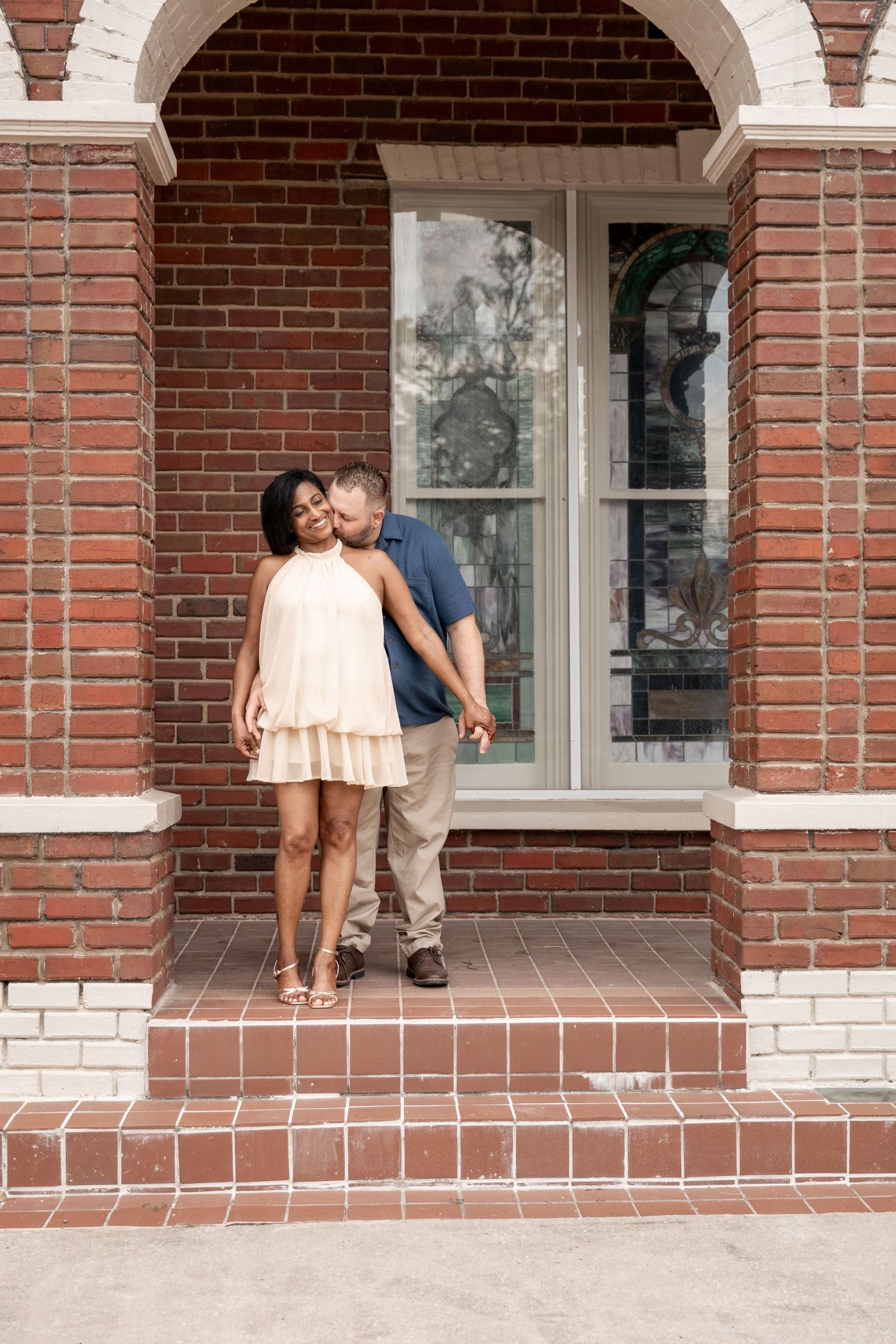 Couple sharing a tender kiss on brick steps of a historic building with stained glass window backdrop. Rockmart, GA