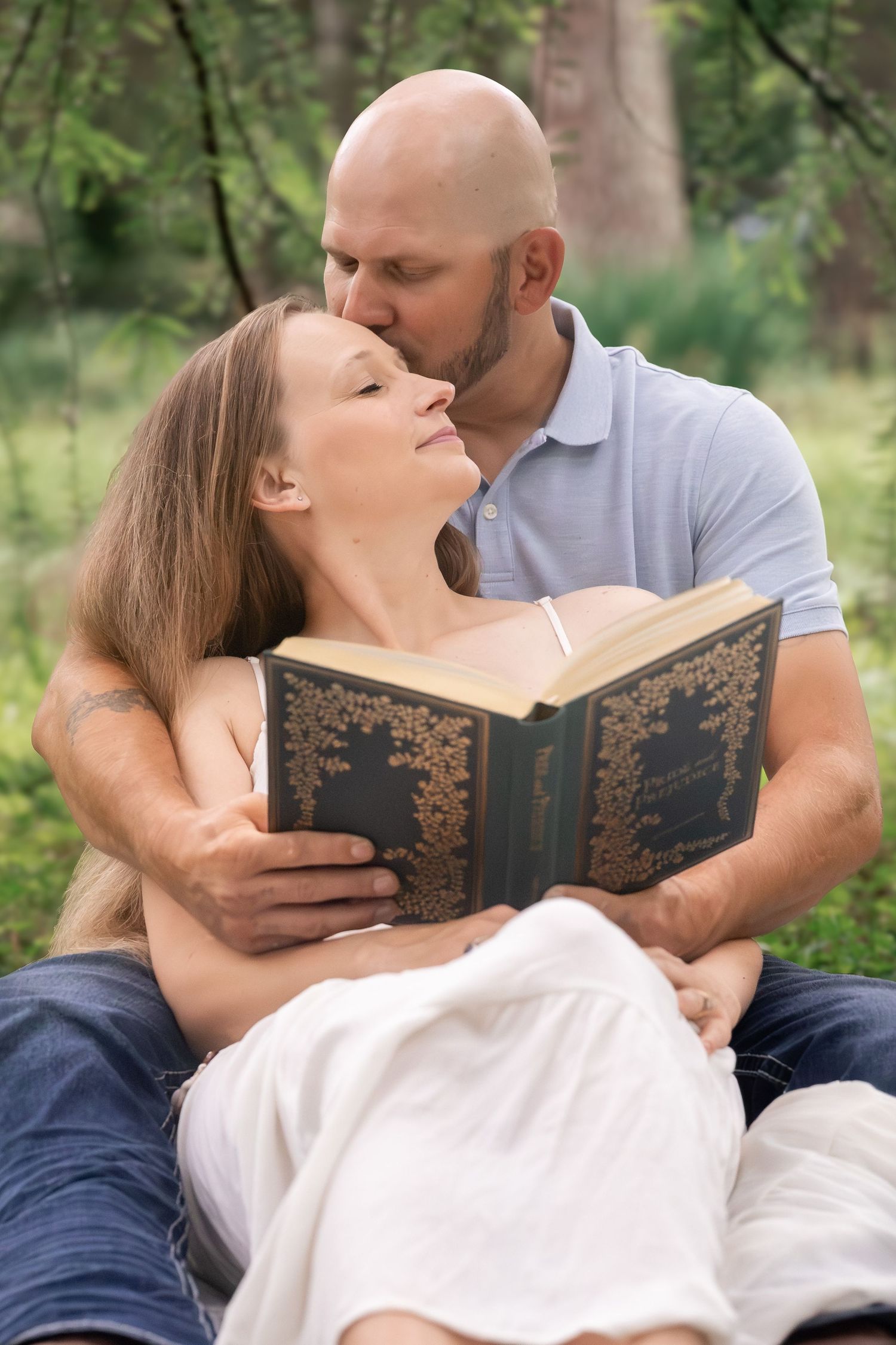 A couple shares a tender moment outdoors, man kissing woman's cheek while she holds an ornate book in a green park. Cedartown, GA