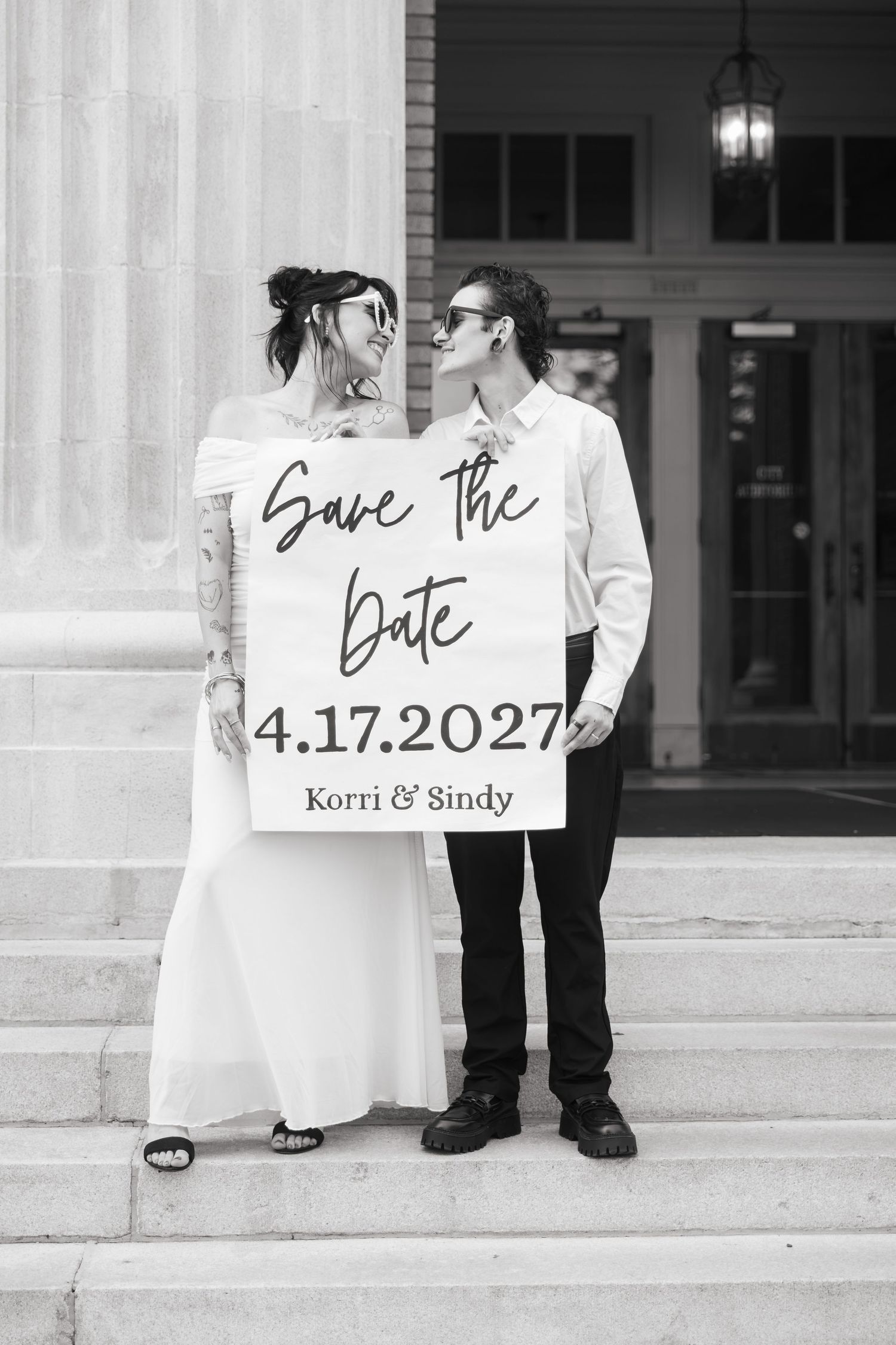 Couple holding Save the Date sign for Korri & Sindy, wedding 4.17.2027, posing on steps in black and white photo. City Hall Rome, GA