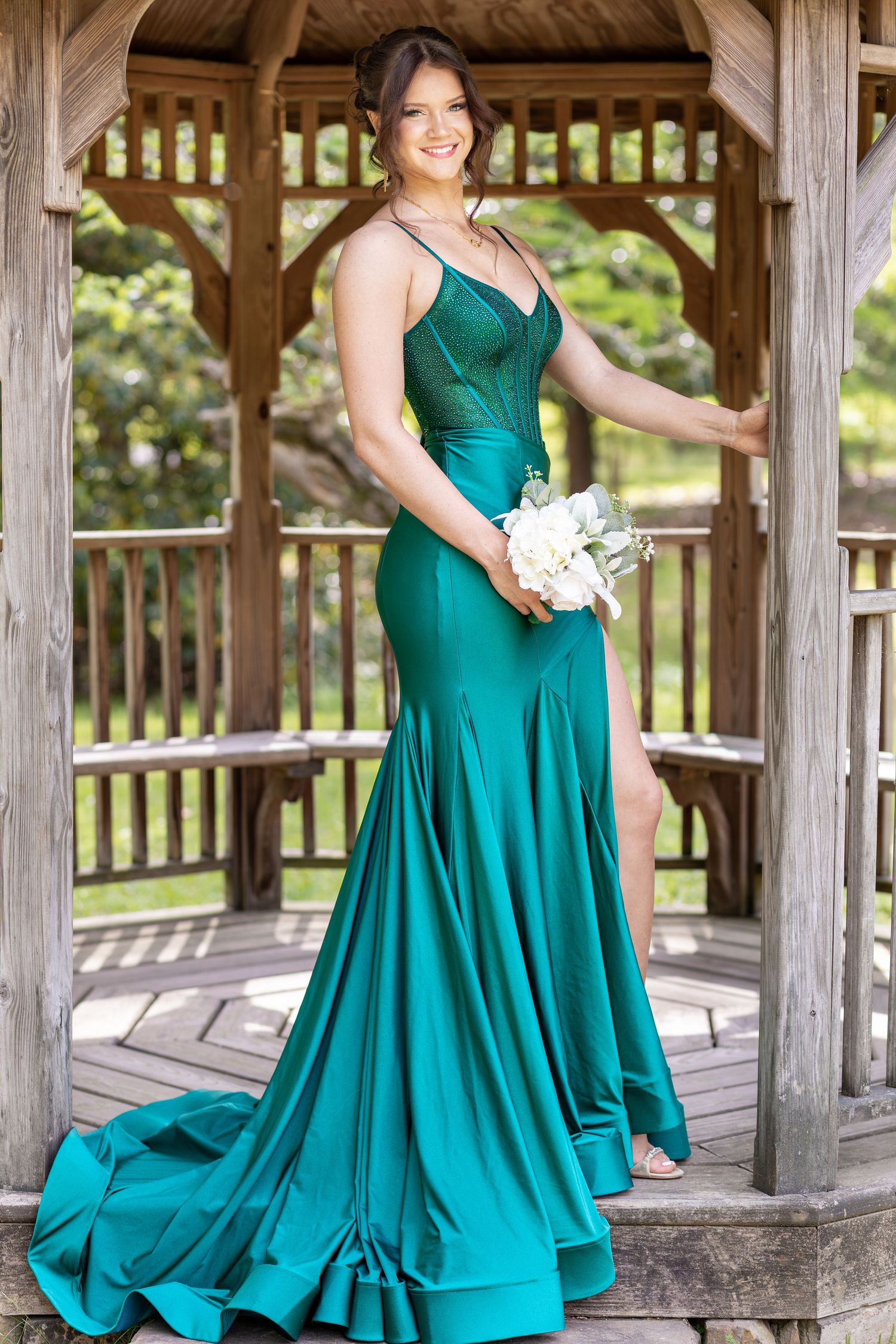 Woman in emerald green mermaid prom gown holding white bouquet, posing in wooden gazebo outdoors at Berry College, Mt Berry Georgia