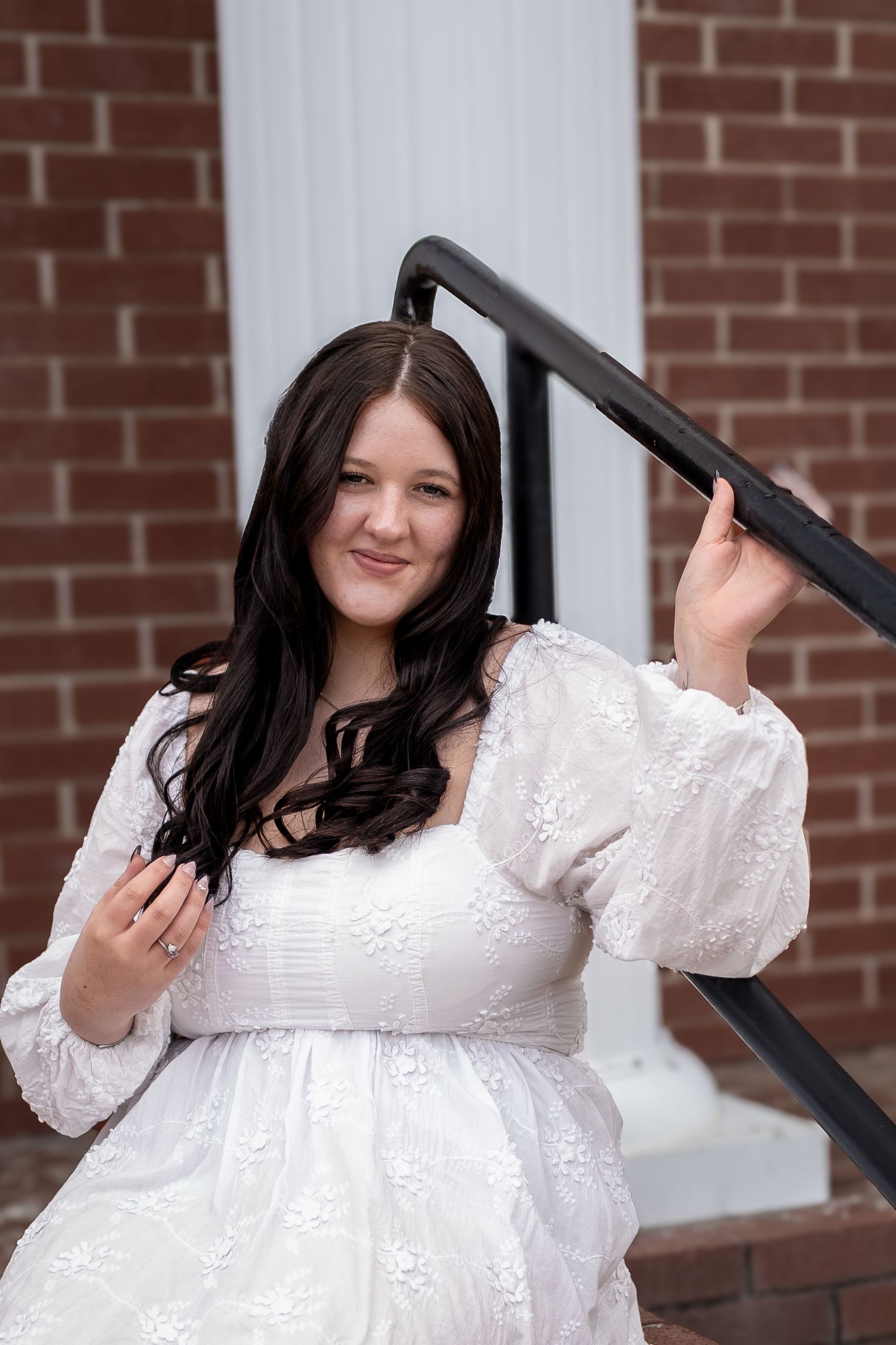 A woman in a white lace dress with long dark hair poses against a brick wall- Cartersville, GA Jessica M Cooper Photography LLC