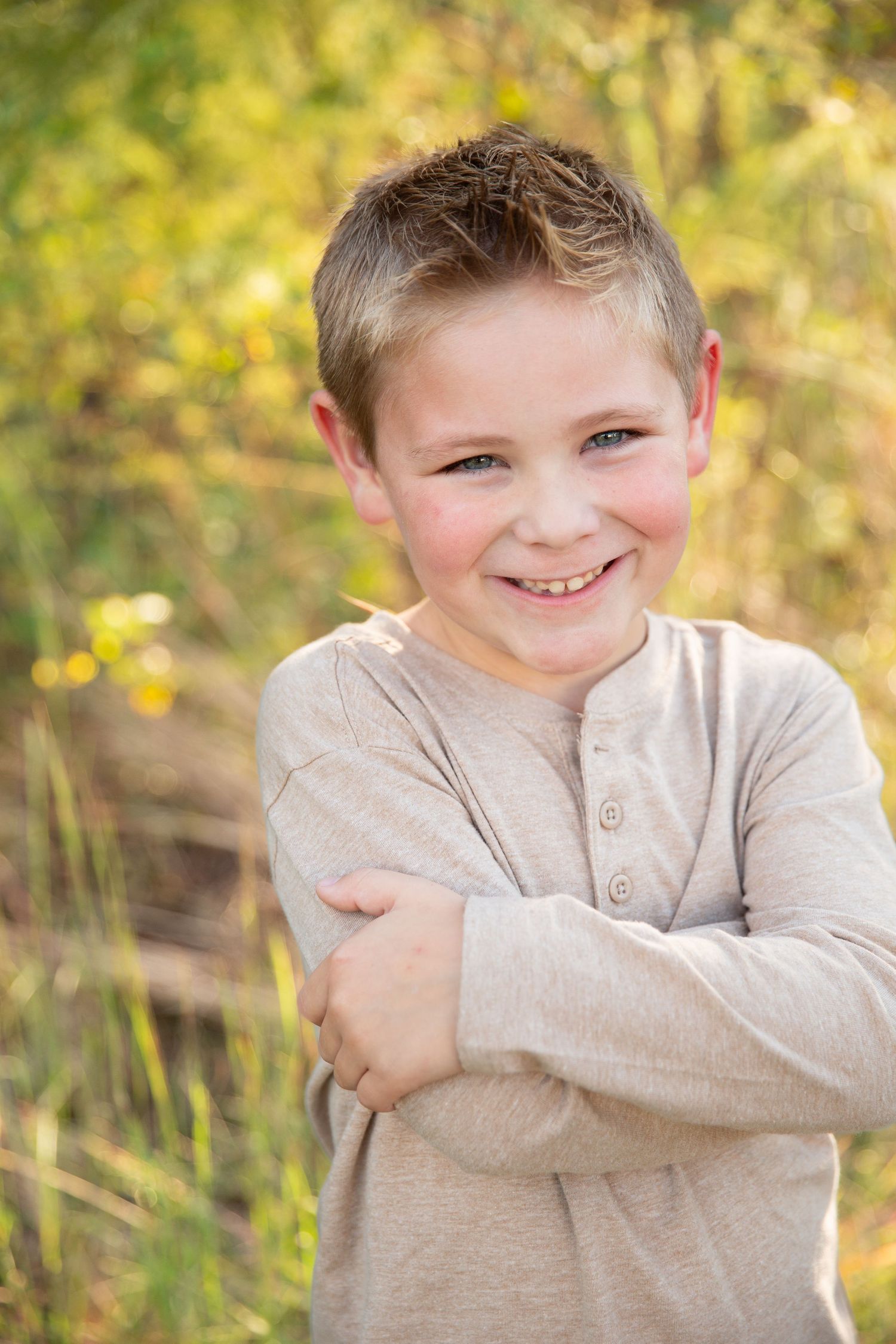A child wearing a beige sweater poses outdoors against a blurred autumn background with golden bokeh lighting effect- Rome GA
