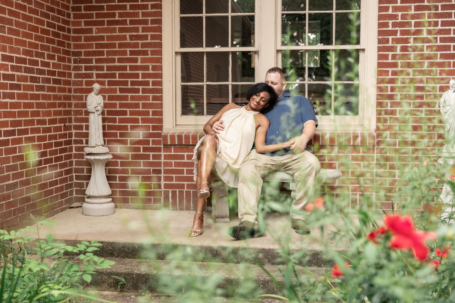 Couple sitting together on brick porch steps surrounded by lush garden greenery and red flowers. Rockmart, GA