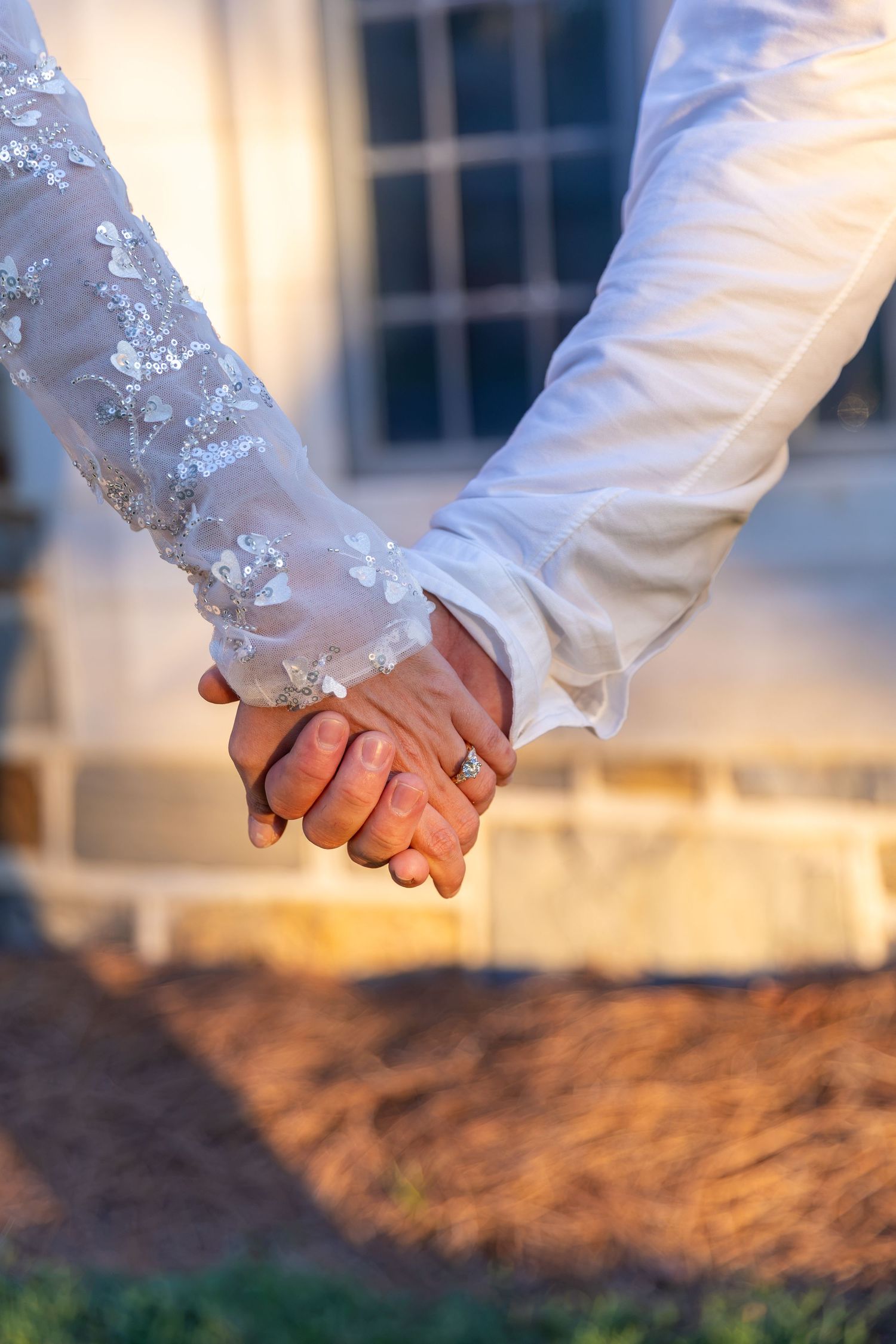 Bride and groom holding hands in wedding attire, bride wearing lace sleeve dress with diamond ring visible. Berry College, Rome, GA