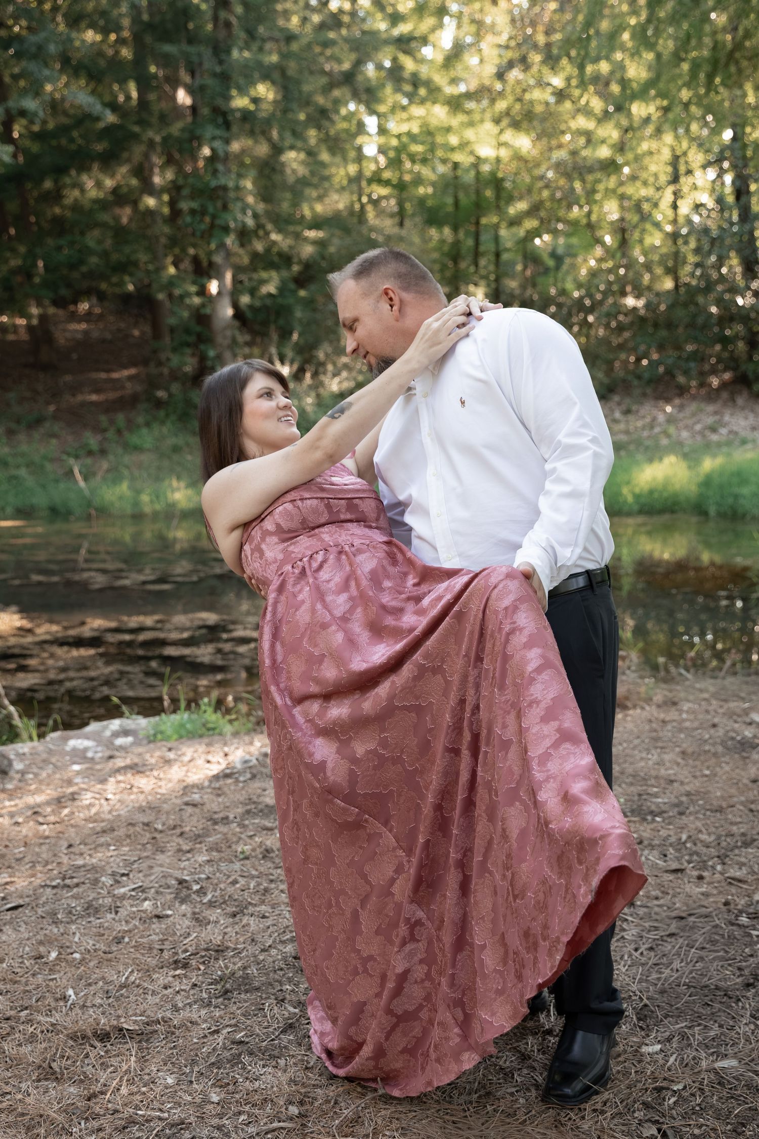 Couple dancing romantically outdoors near a forest pond, woman in pink gown, man in white shirt and black pants. Berry College, Rome, GA