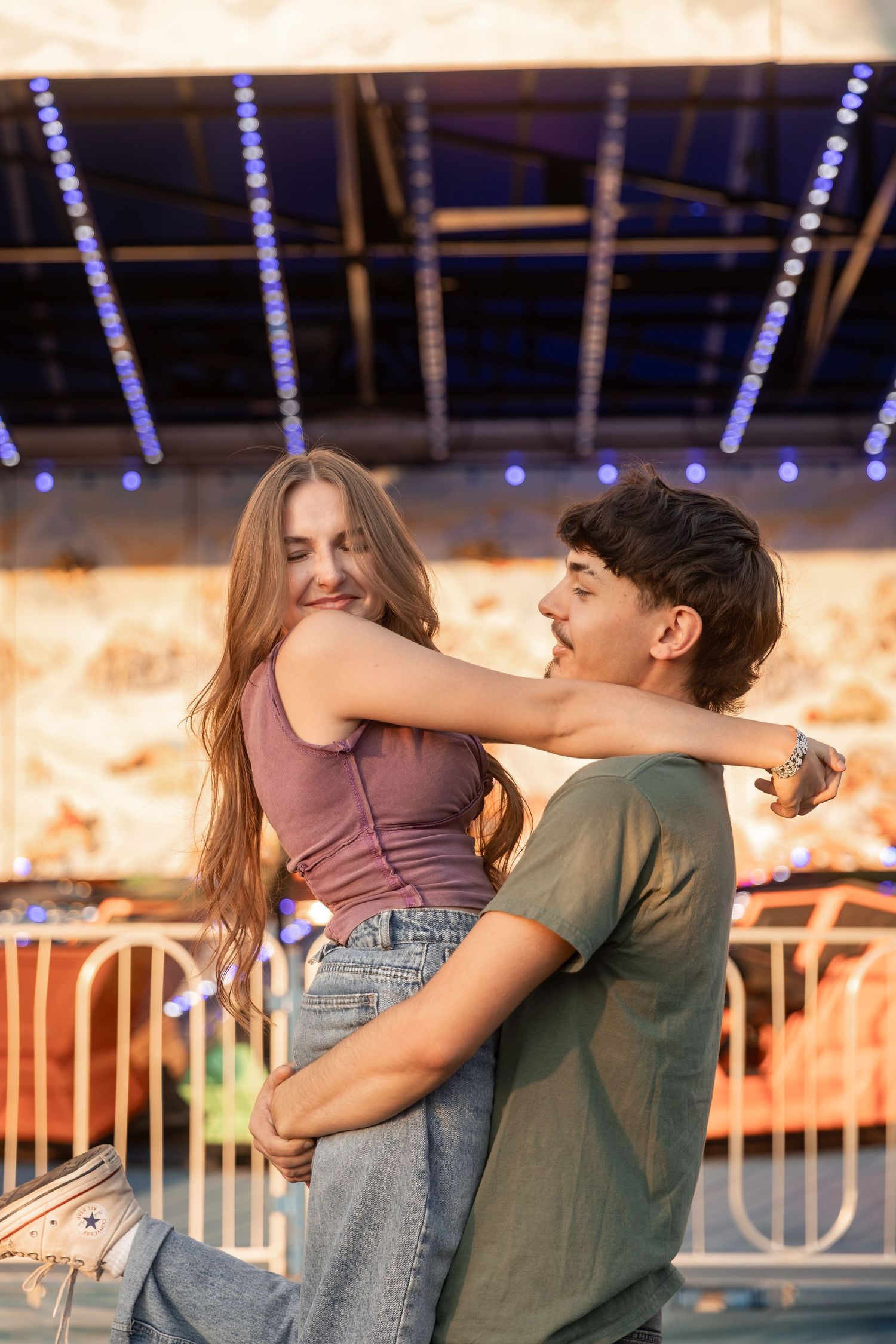 A young couple embracing and laughing together at a colorful amusement park at night.