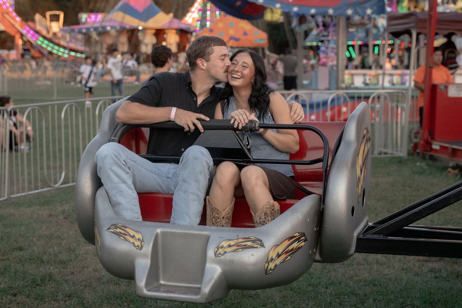 Couple laughing together on a carnival ride at an outdoor fair at dusk.
