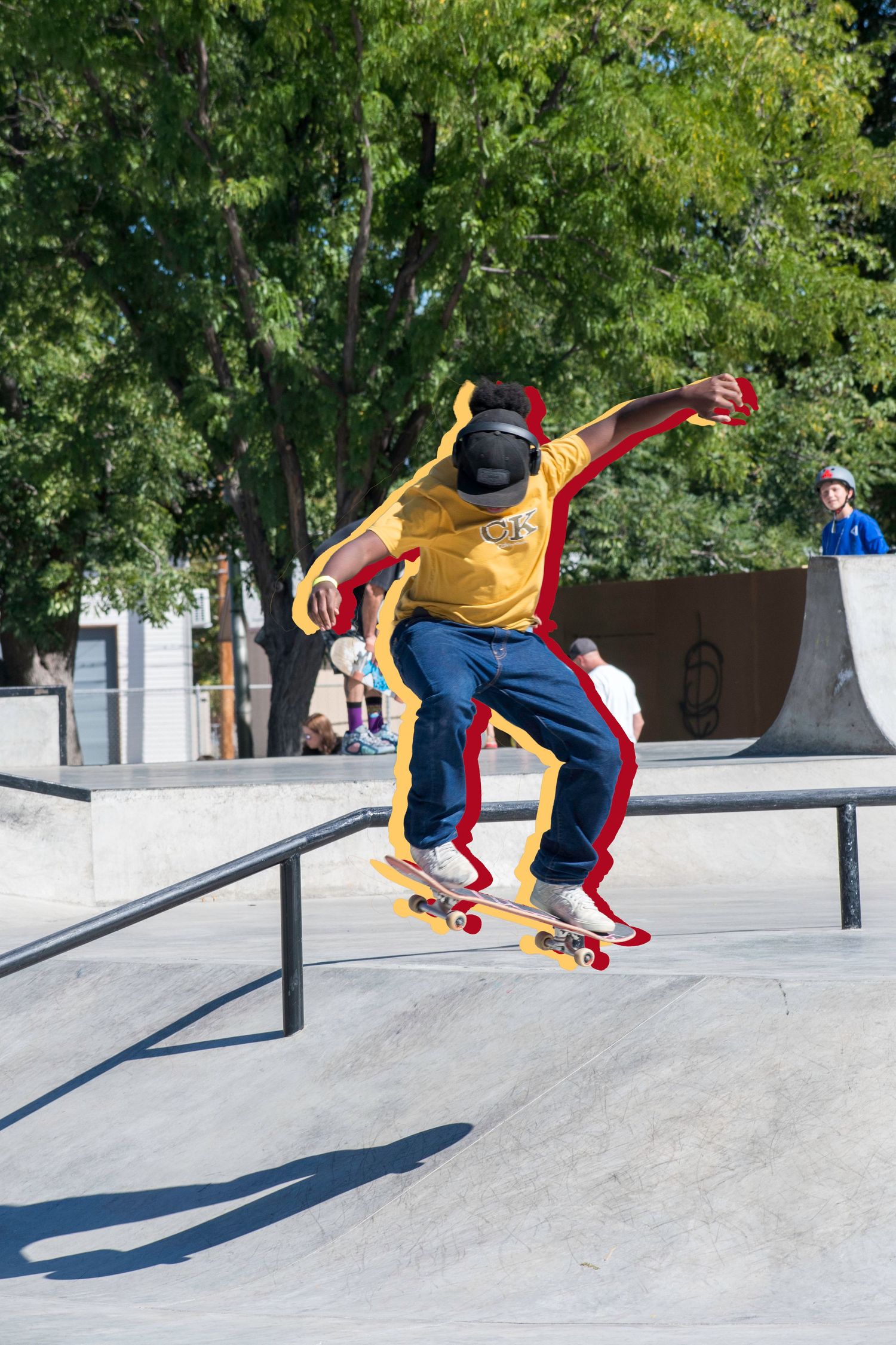 Skateboarder in yellow shirt and jeans performing a trick at an outdoor skate park on a sunny day.