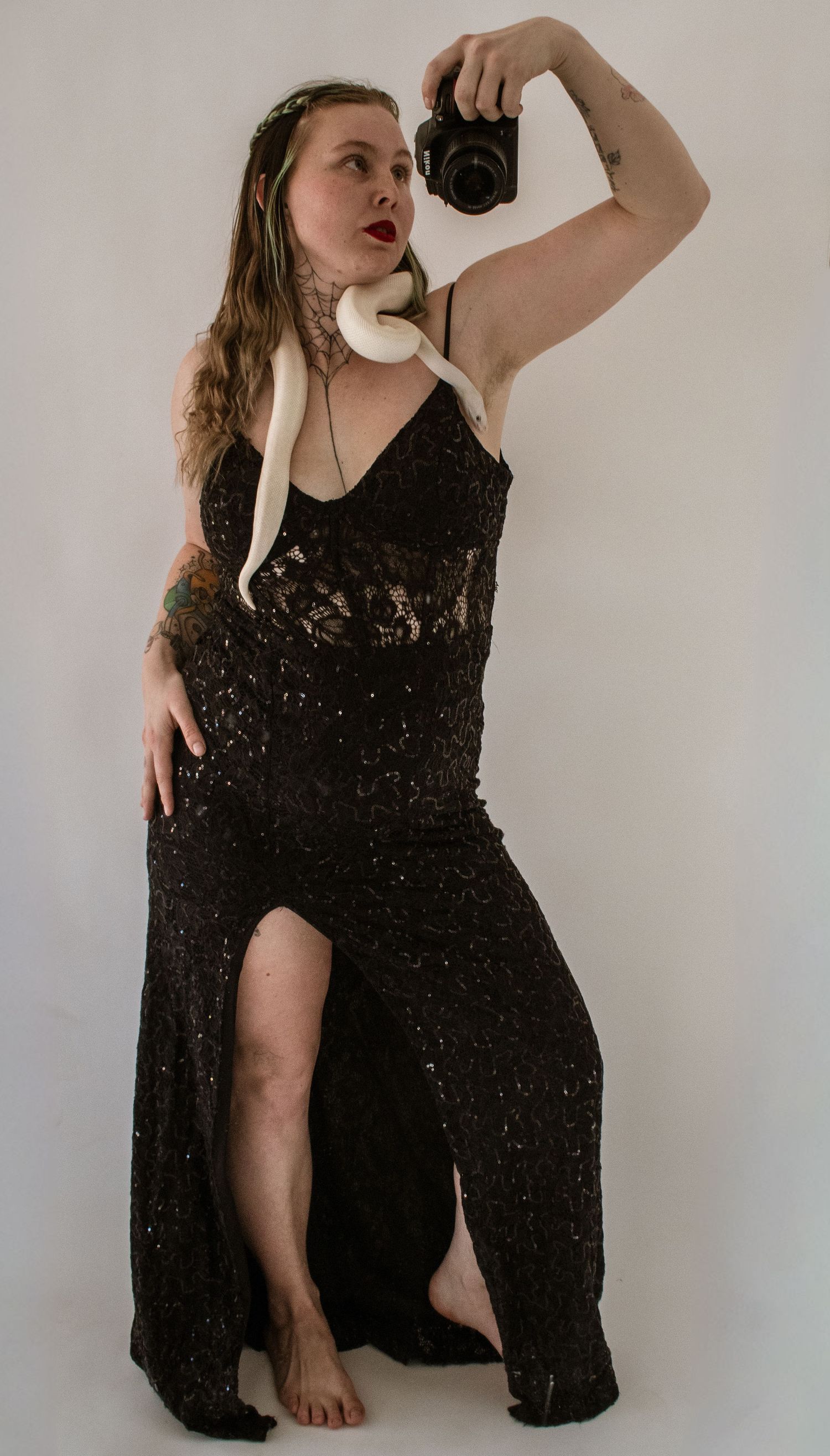Woman in black lace gown holding camera with white albino snake draped around neck.