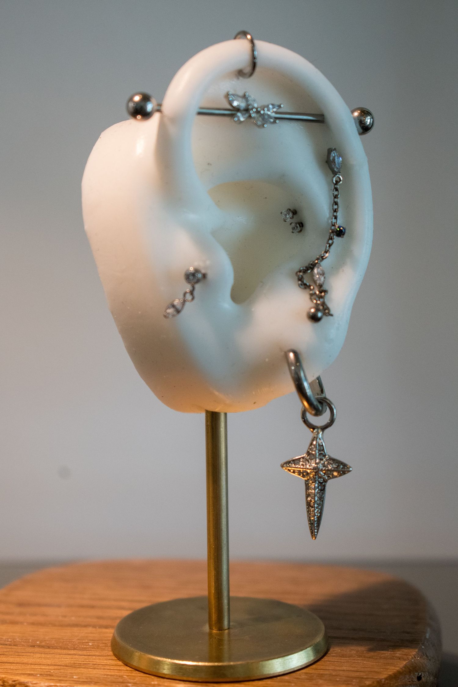 White ceramic ear display stand on gold base showcasing multiple silver piercings including cross charm and industrial bar.