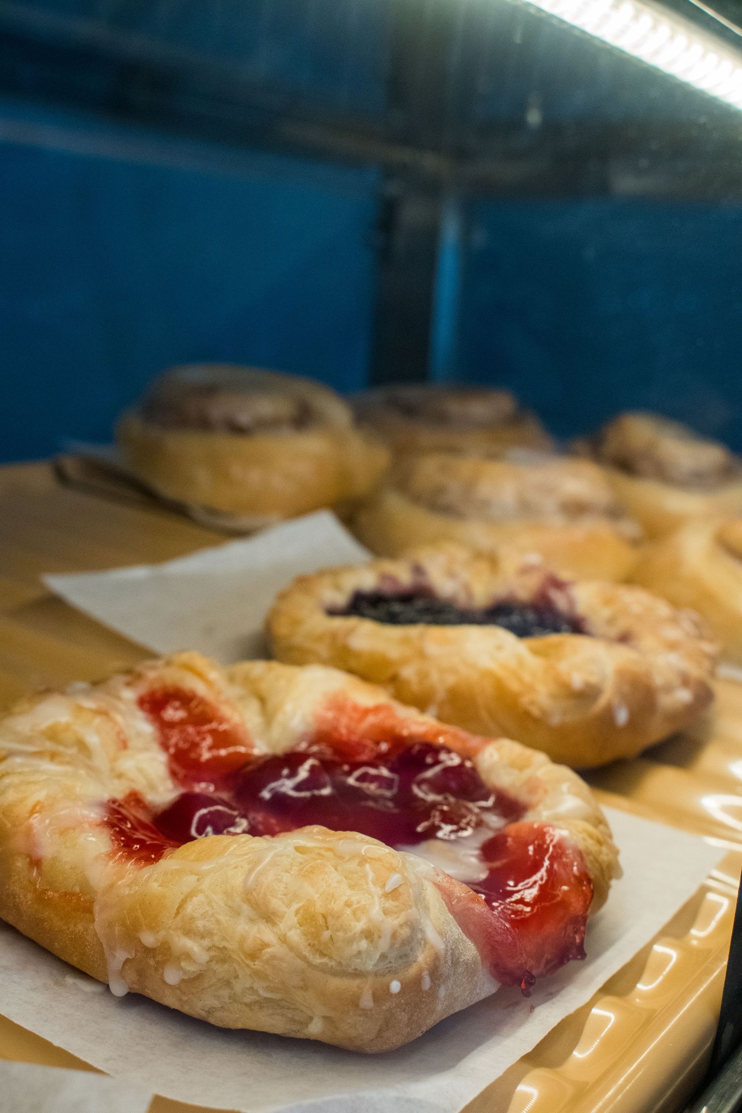 Freshly baked Danish pastries with cherry and blueberry filling displayed on parchment paper in a bakery case.
