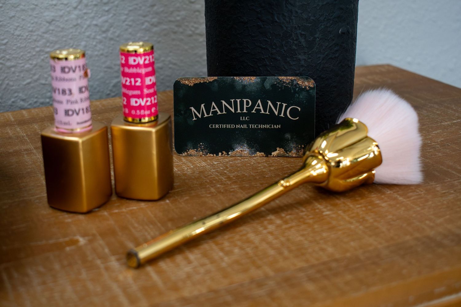Gold rose makeup brush and Manipanic card beside two gold lipsticks on a wooden surface.