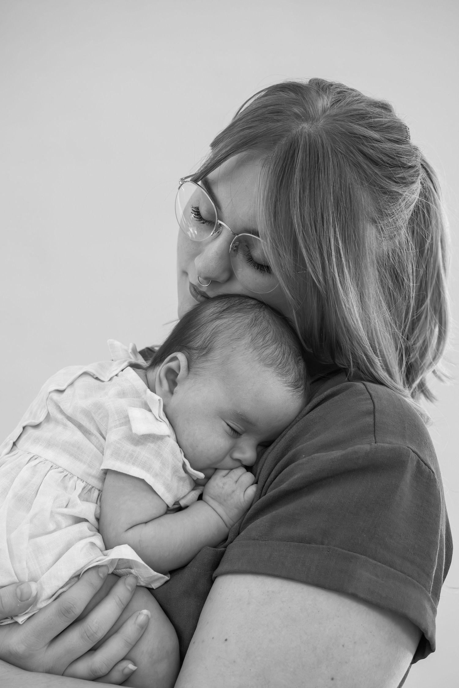 Black and white photo of mother kissing sleeping newborn baby held against her chest.