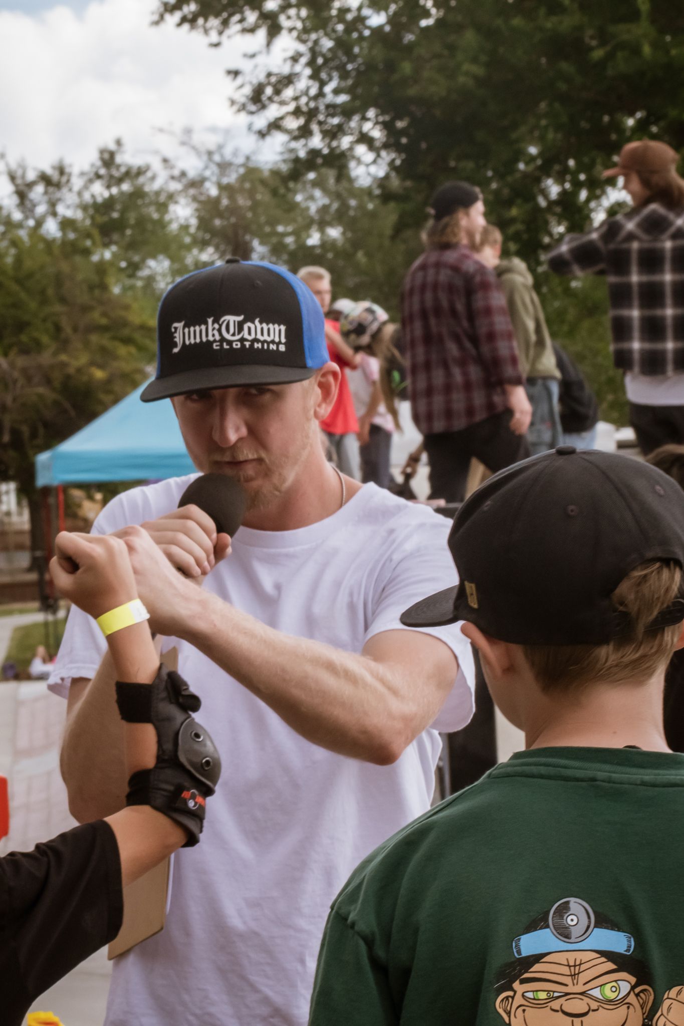 Man in JunkTown snapback hat signing autograph for young fan at outdoor skateboarding event.