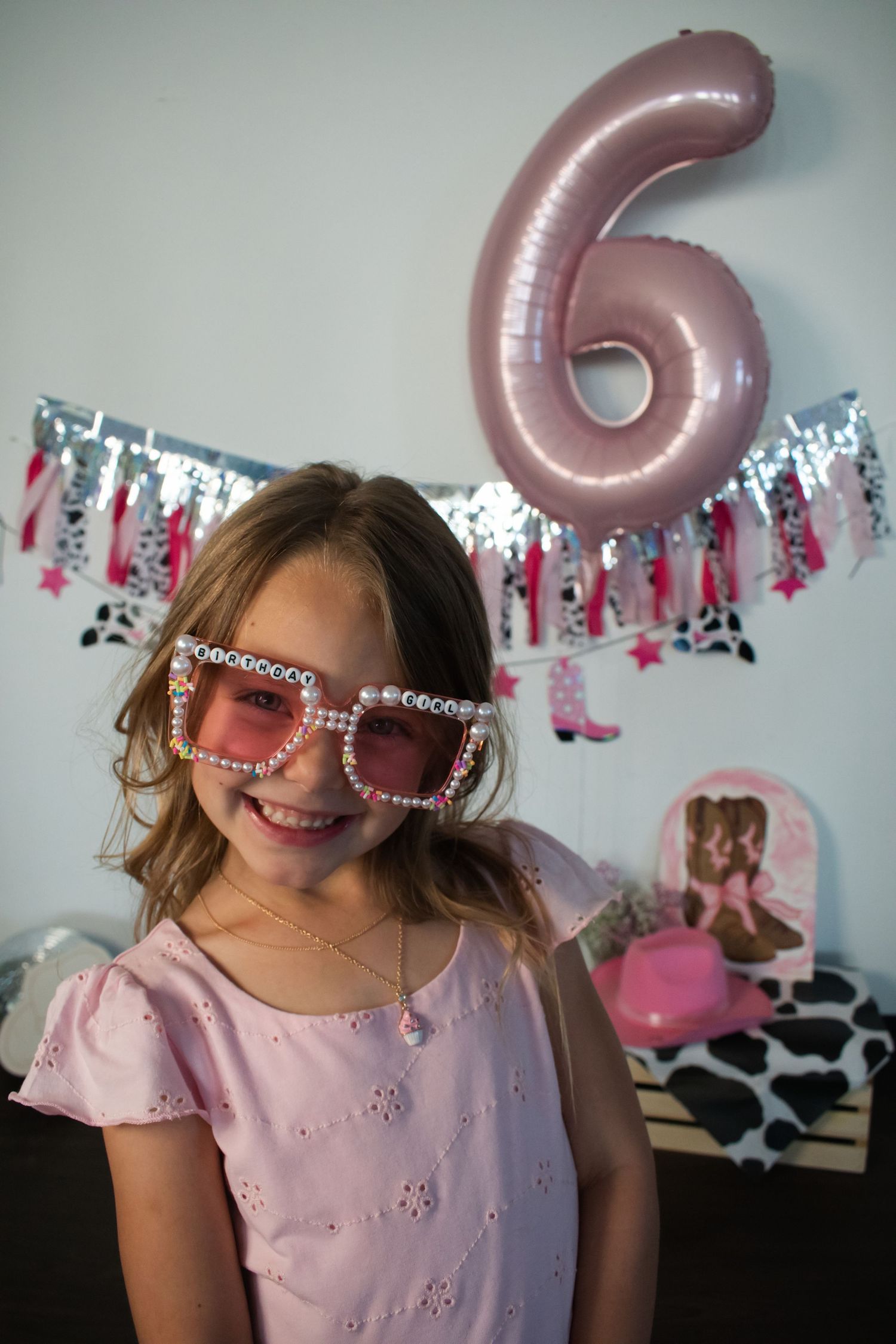 Smiling girl wearing pink rhinestone sunglasses celebrating her 6th birthday with cowgirl themed decorations.