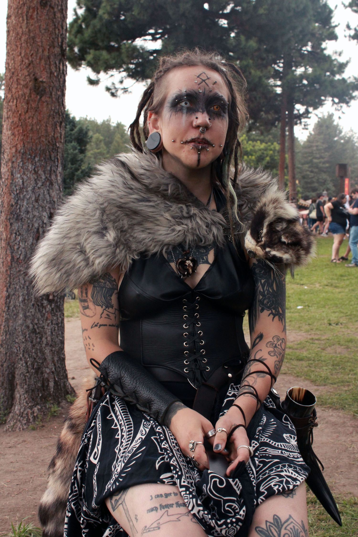 Woman in Viking cosplay with face paint, fur shawl, corset, and tattoos at an outdoor festival.