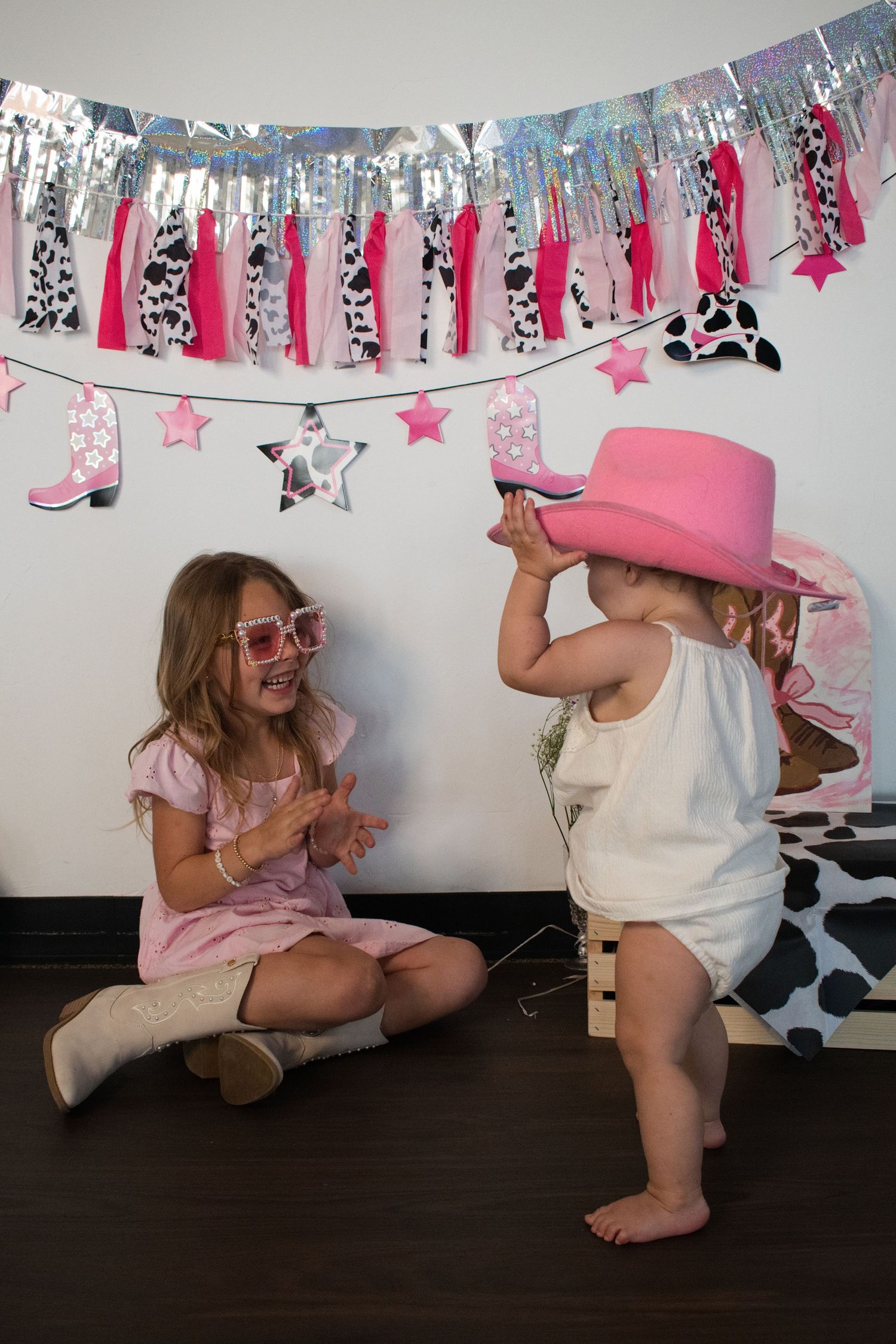 Two young sisters playing together at a pink cowgirl themed birthday party with festive decorations.