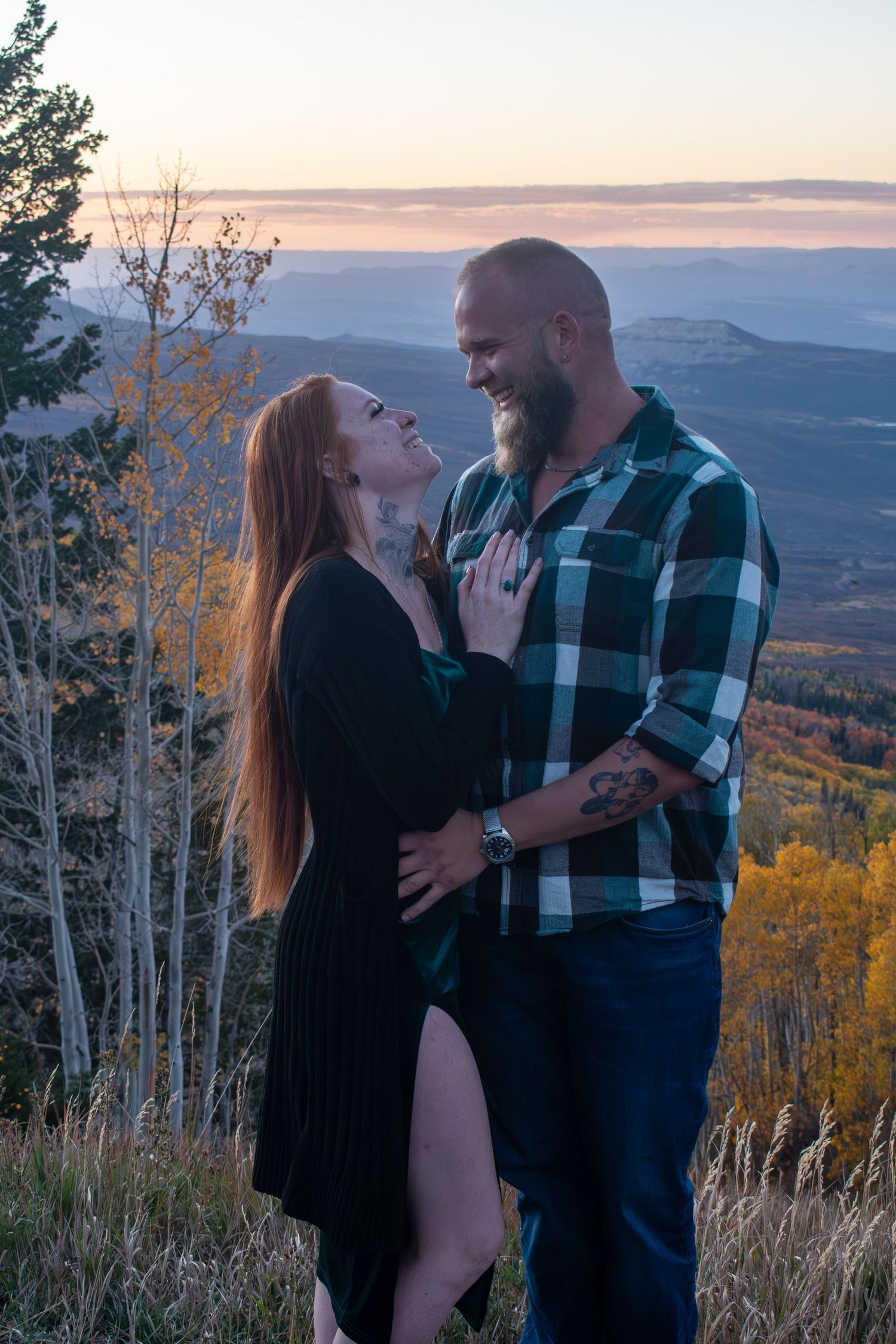 Couple embracing and laughing at sunset on a mountain overlook, surrounded by autumn foliage.