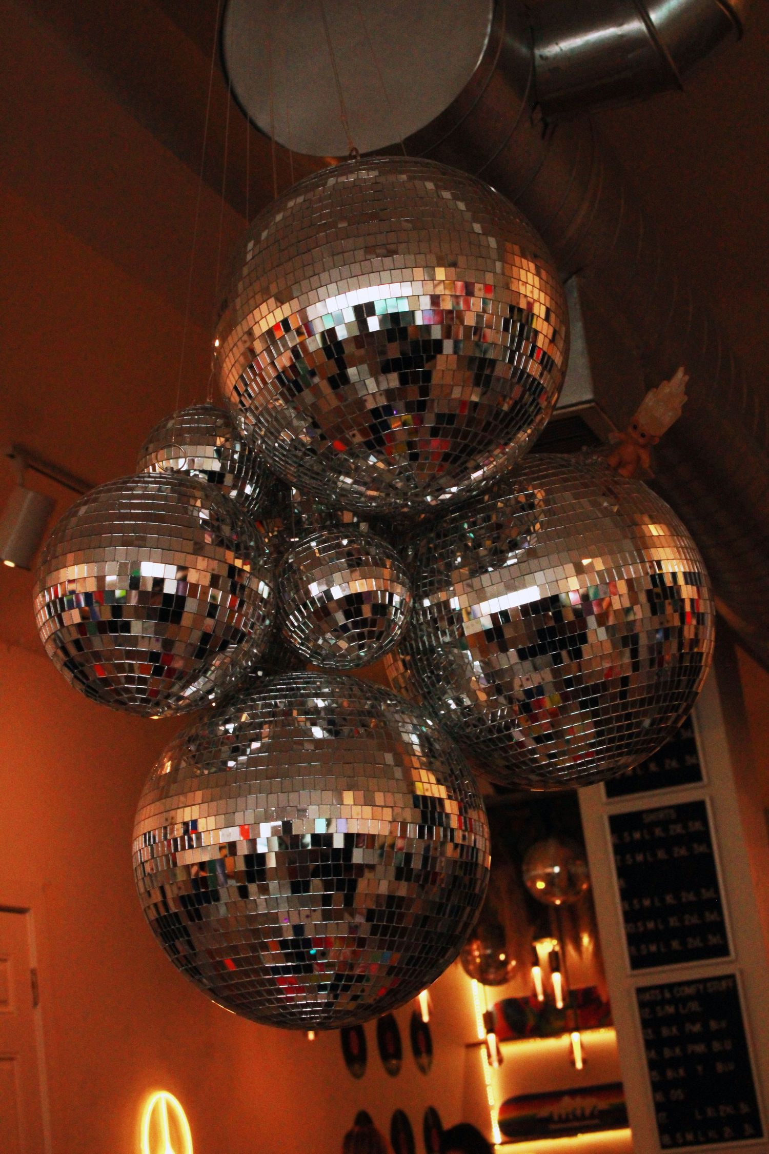 Cluster of five large silver mirror disco balls hanging from ceiling in warmly lit venue.