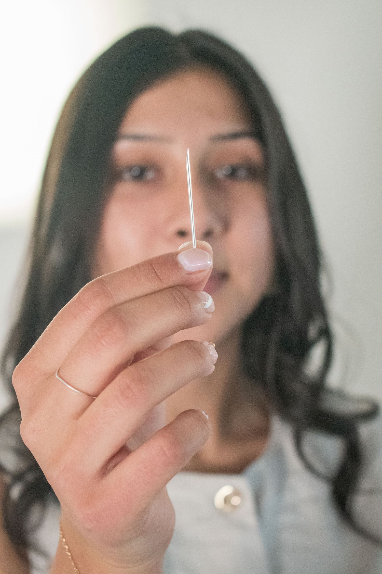 Young woman with dark hair holding cotton swab close to camera in soft light.