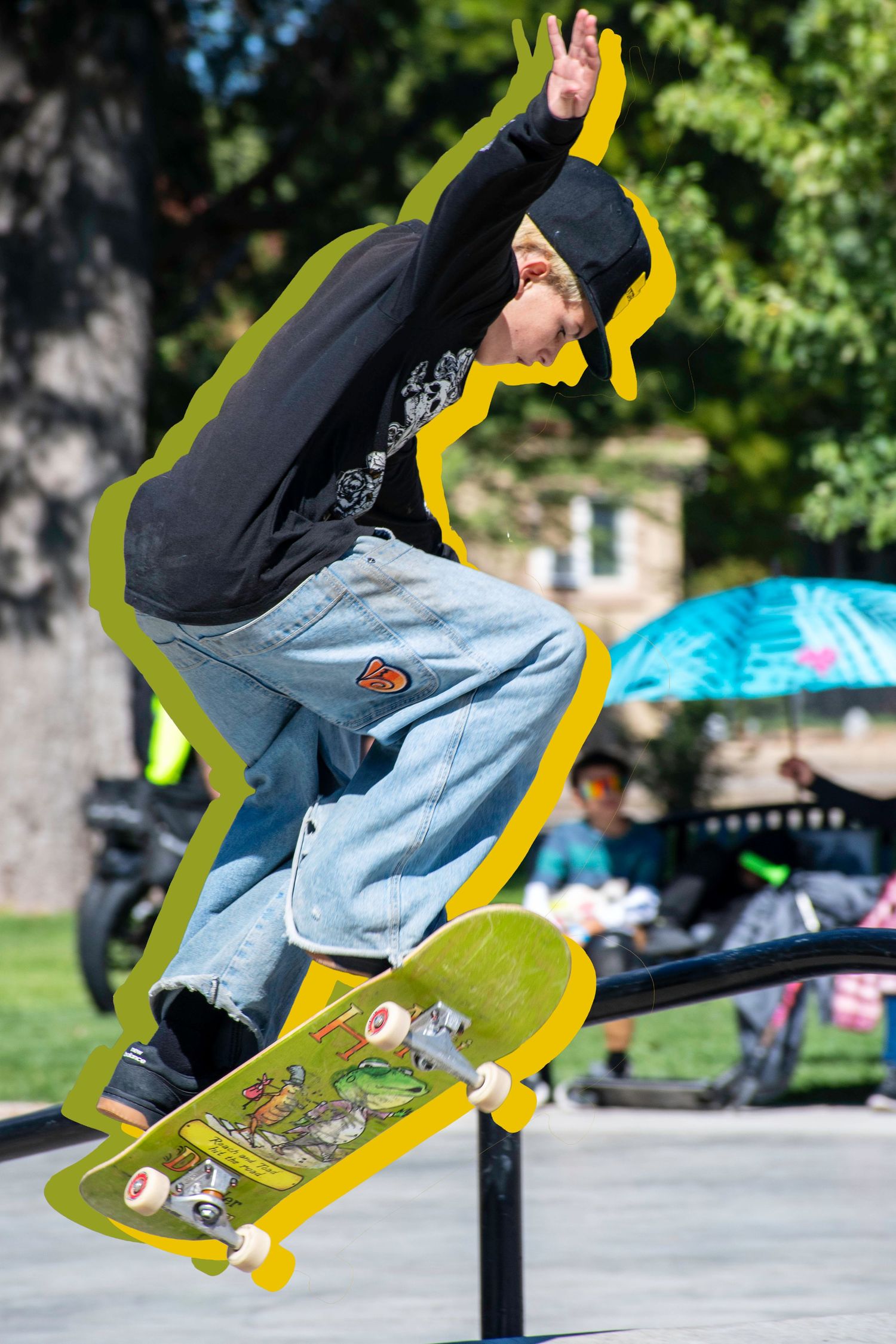 Skateboarder performing a trick on a yellow skateboard at an outdoor skate park on a sunny day.
