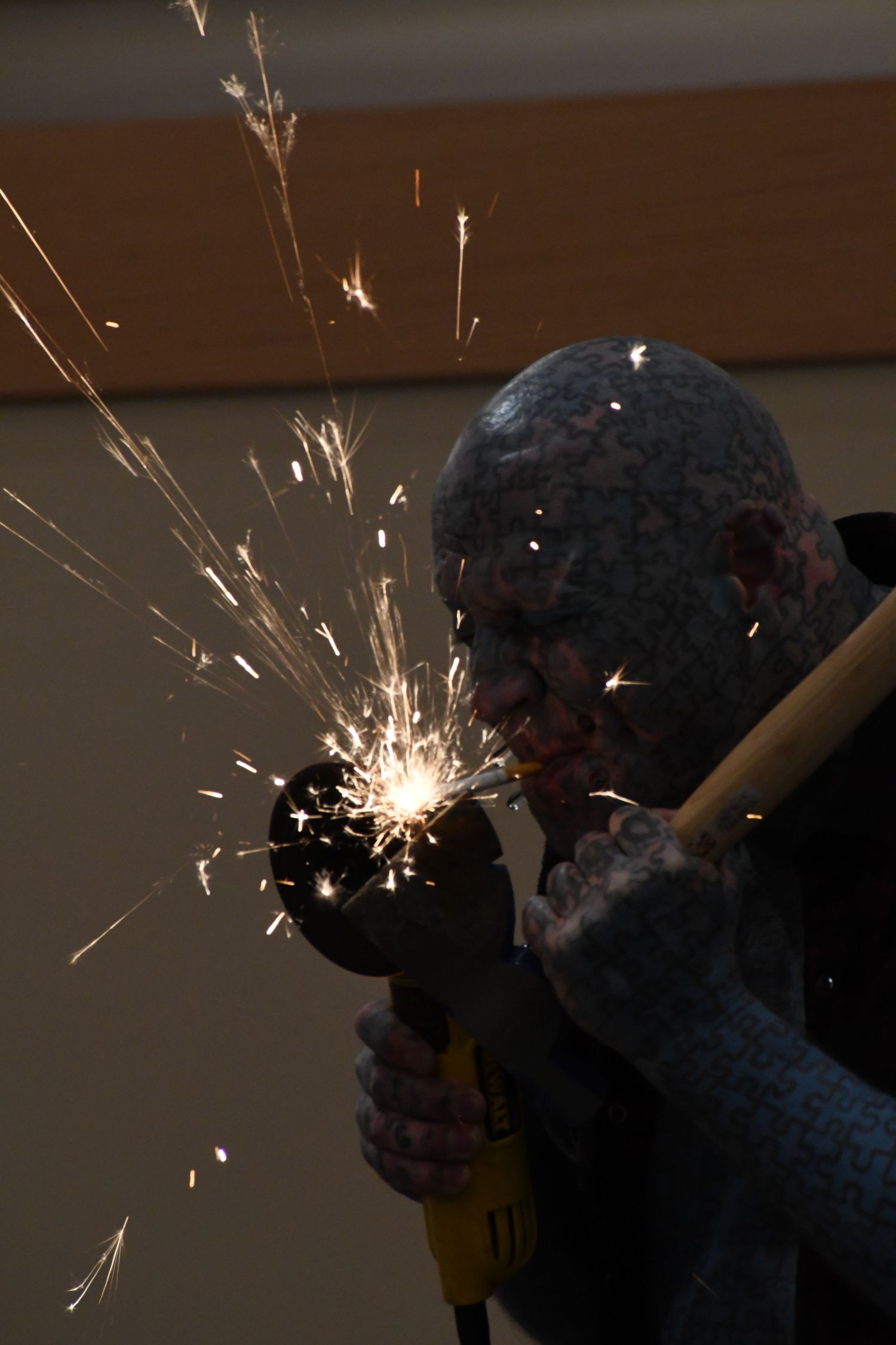 Worker using an angle grinder with bright sparks flying, wearing protective gear in a dark workshop setting.
