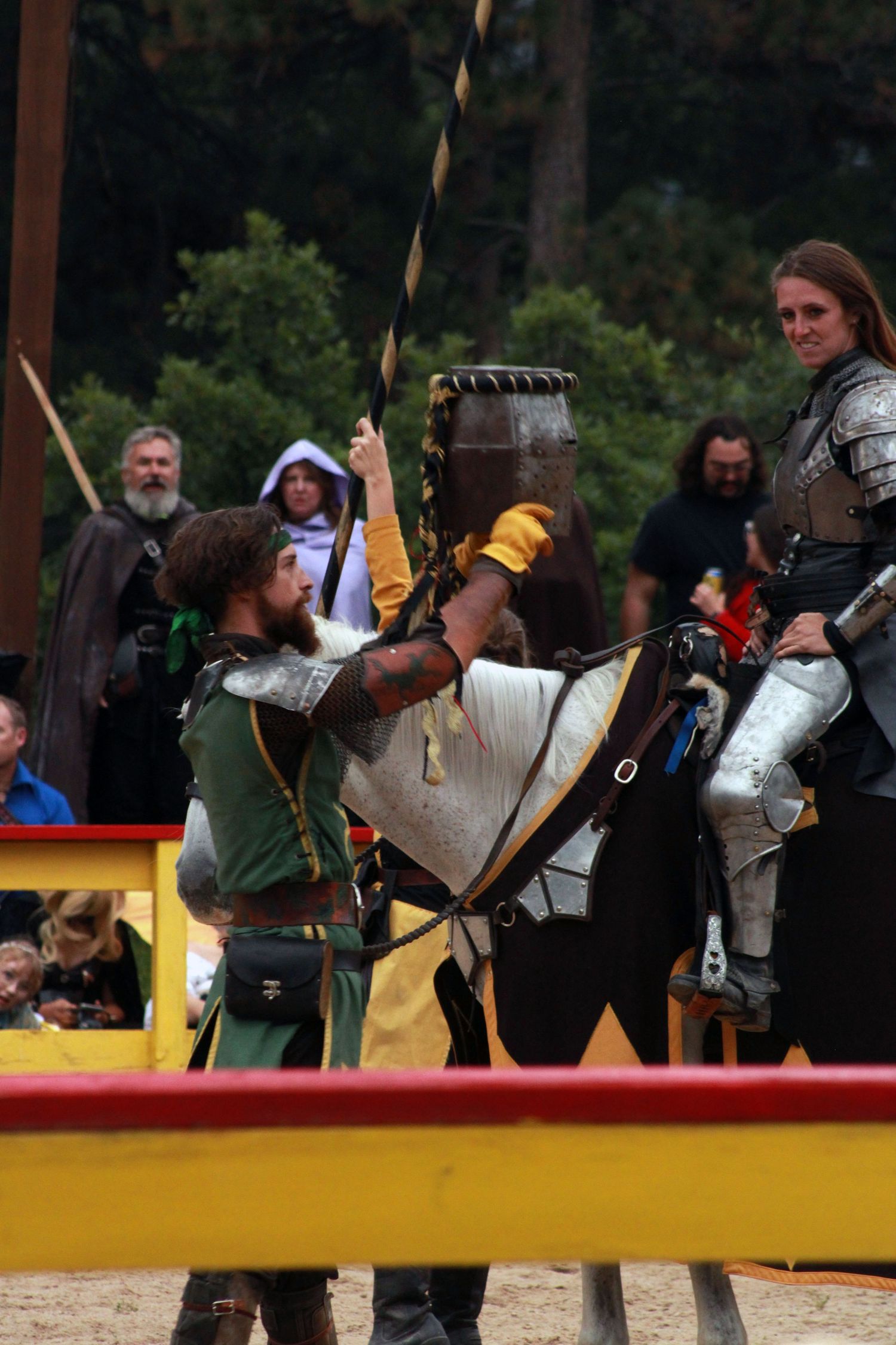 Medieval jousting tournament with armored knight on horseback and performer in green costume at Renaissance faire.