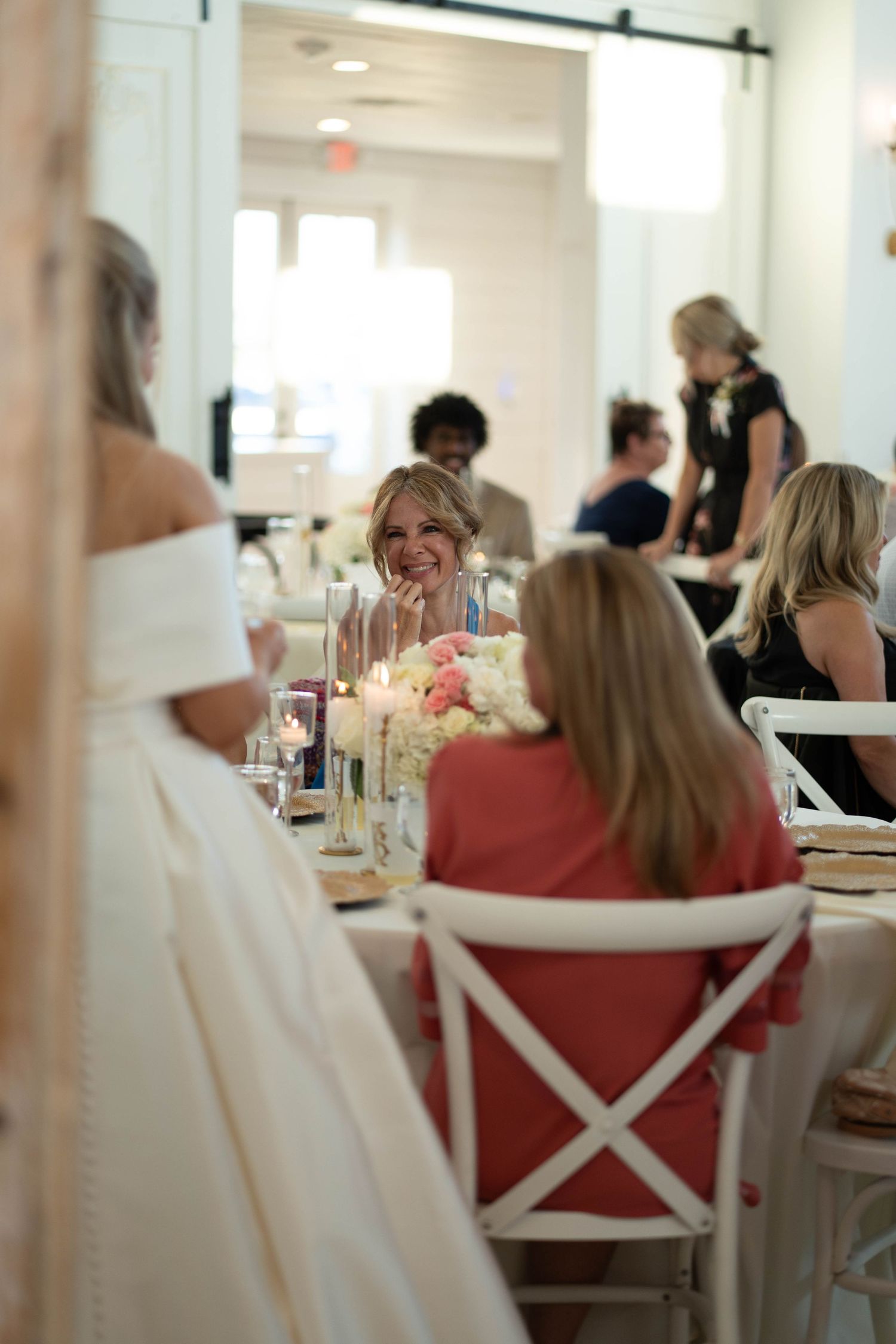 Wedding reception tables set with white chairs and elegant decor in a bright indoor venue.
