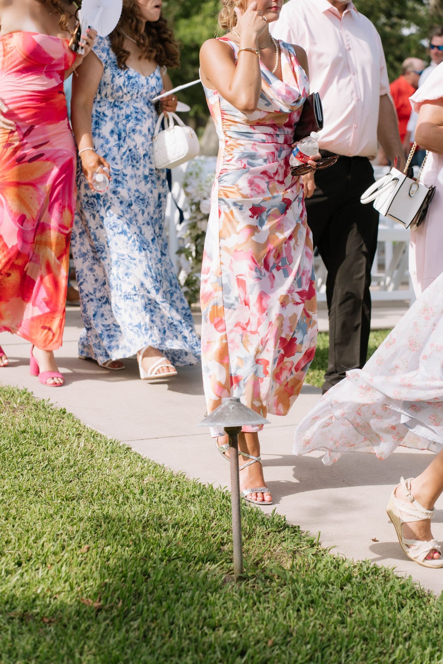Wedding guests in colorful floral dresses walking on a garden pathway.