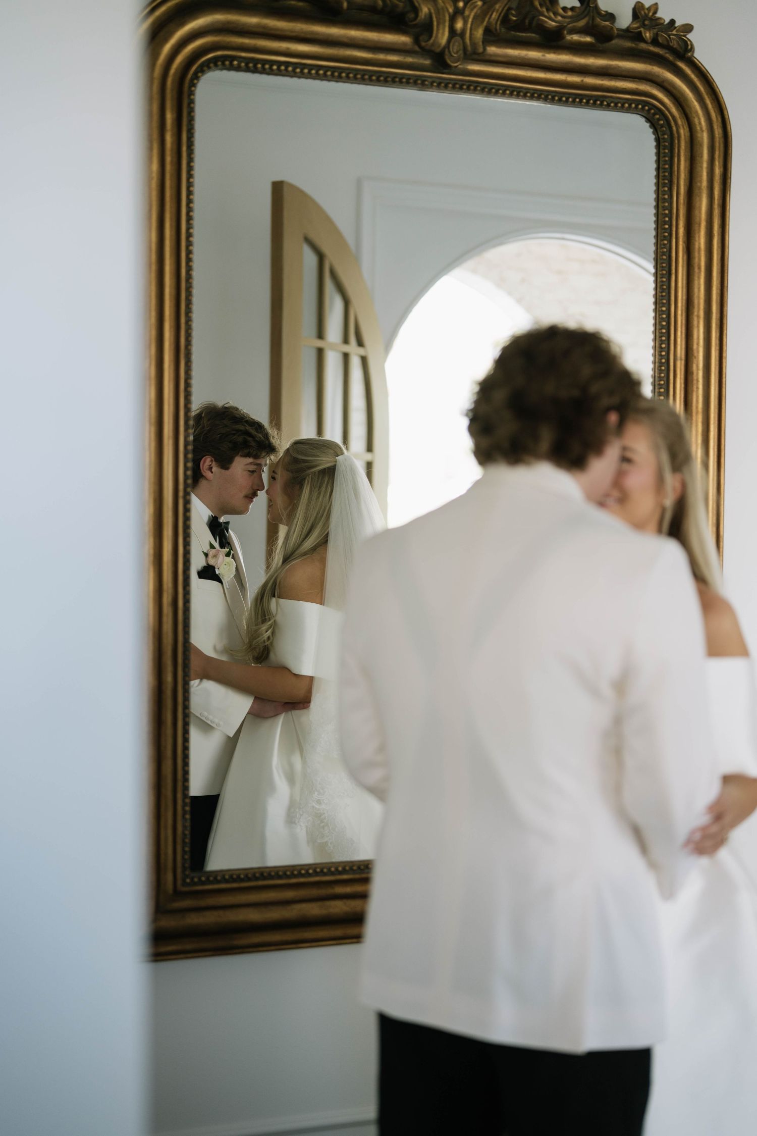 Elegant gold-framed mirror reflection in bright white room.