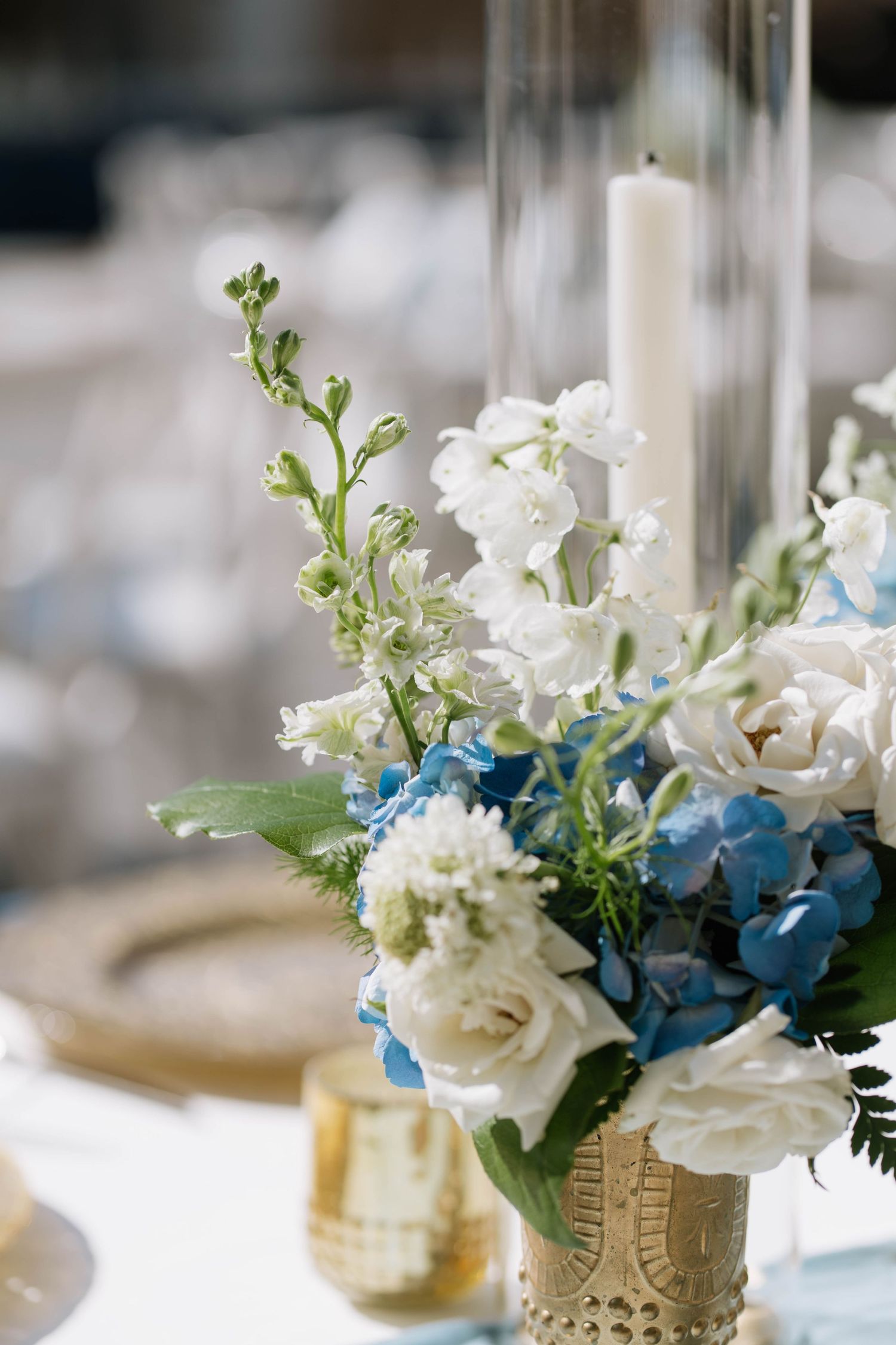 Elegant centerpieces featuring white and blue flowers in gold mercury glass vases.