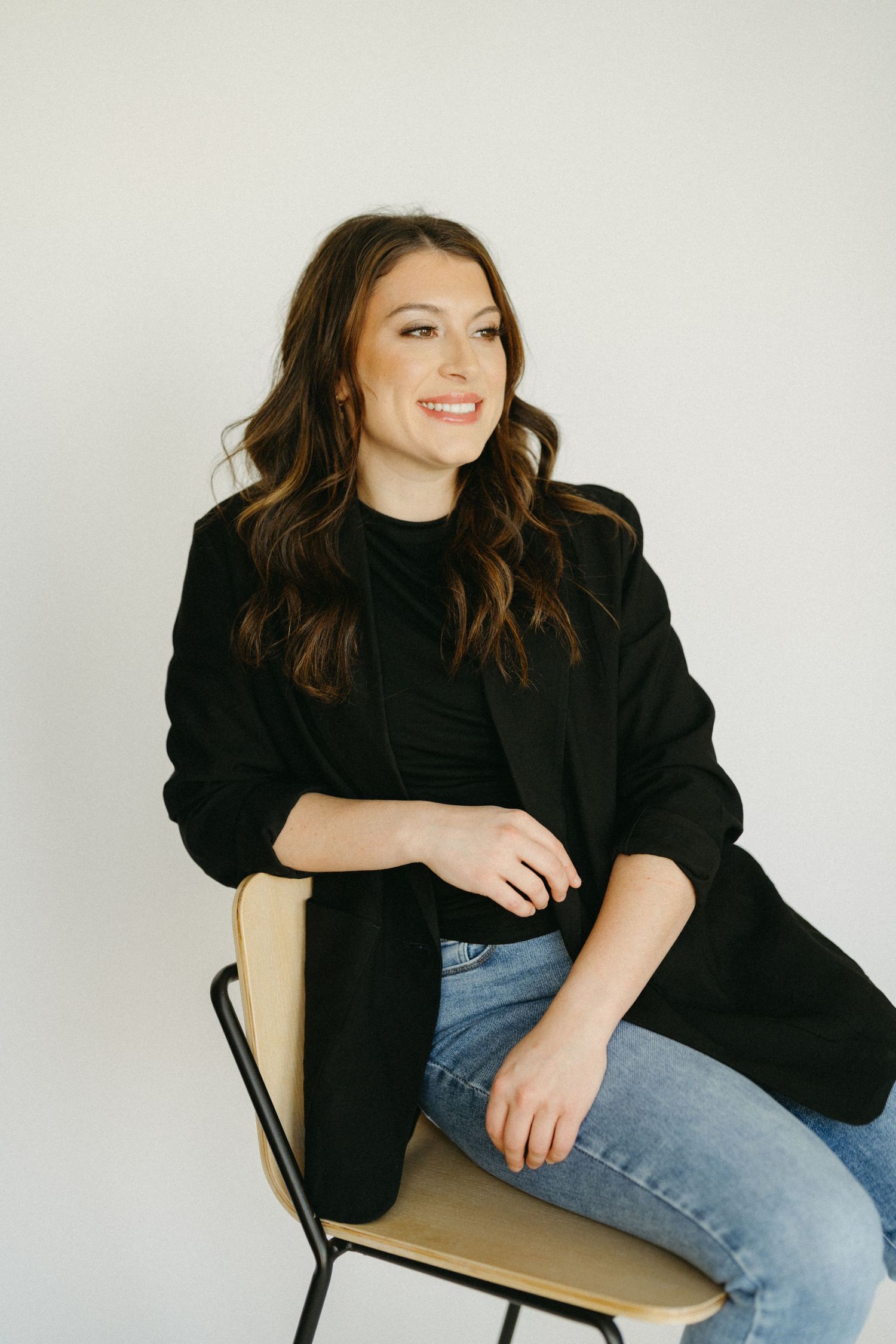 Fashion portrait series of a person in a black turtleneck and jeans posing casually on a chair against white background.