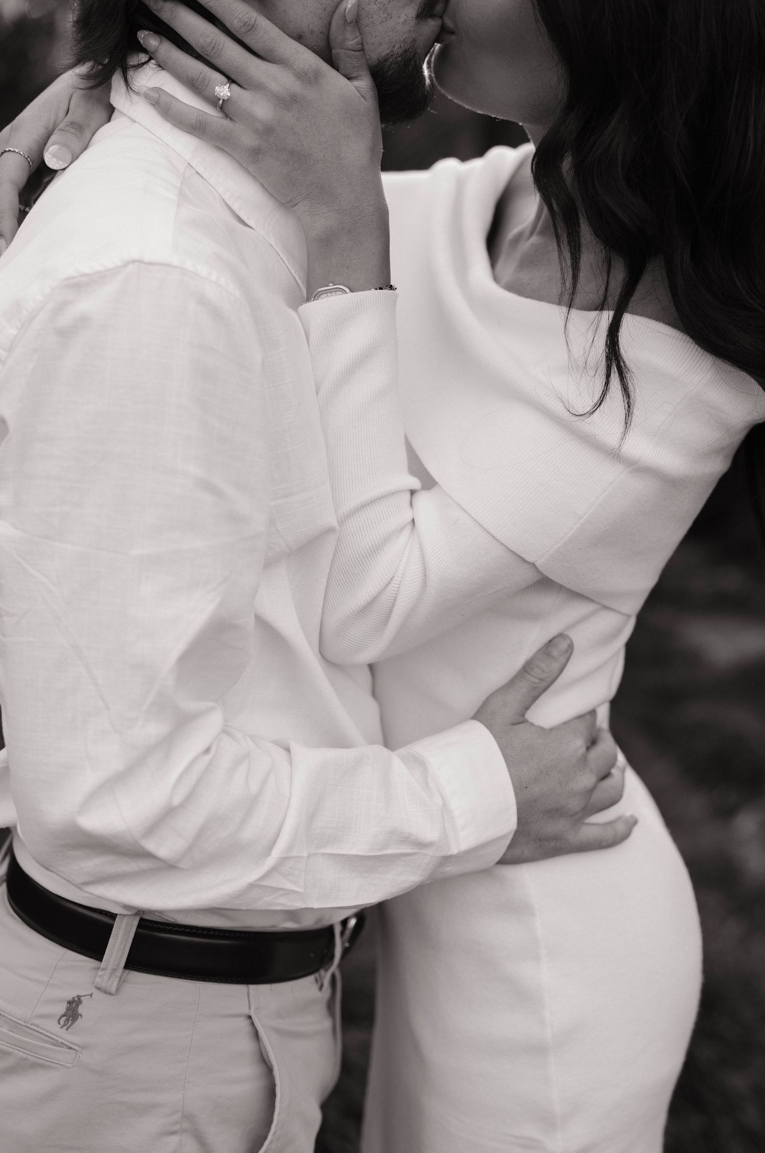 Intimate black and white photo of couple in matching white outfits embracing.