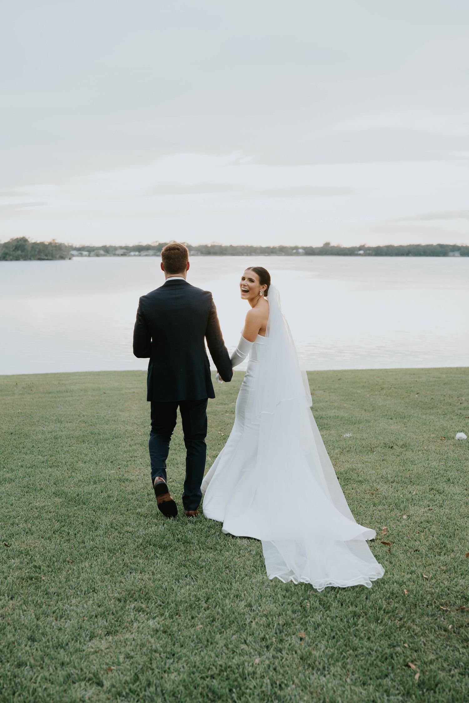 A newlywed couple stands together overlooking a serene lake on their wedding day.