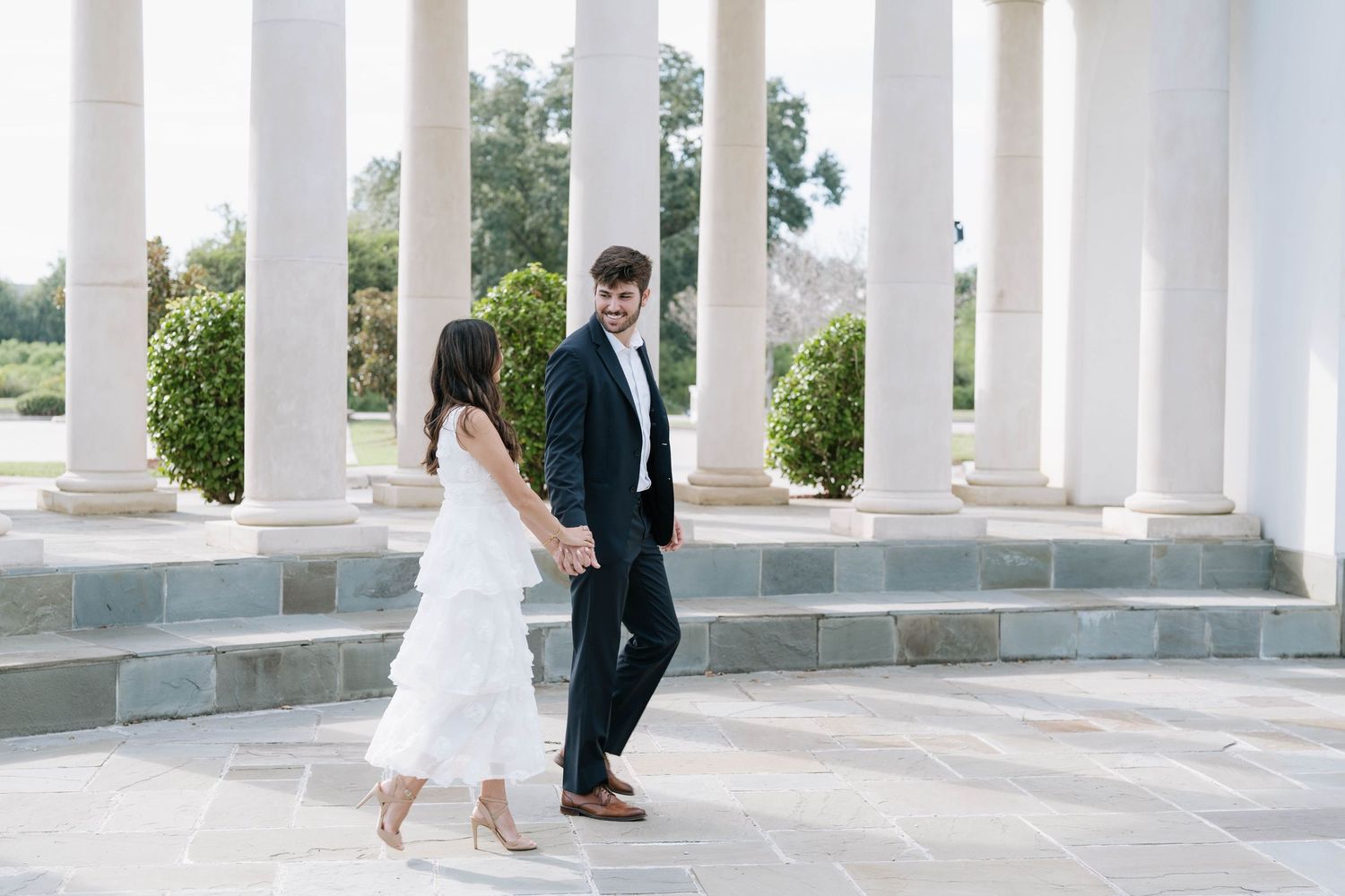 Wedding party poses between elegant white columns at outdoor venue.