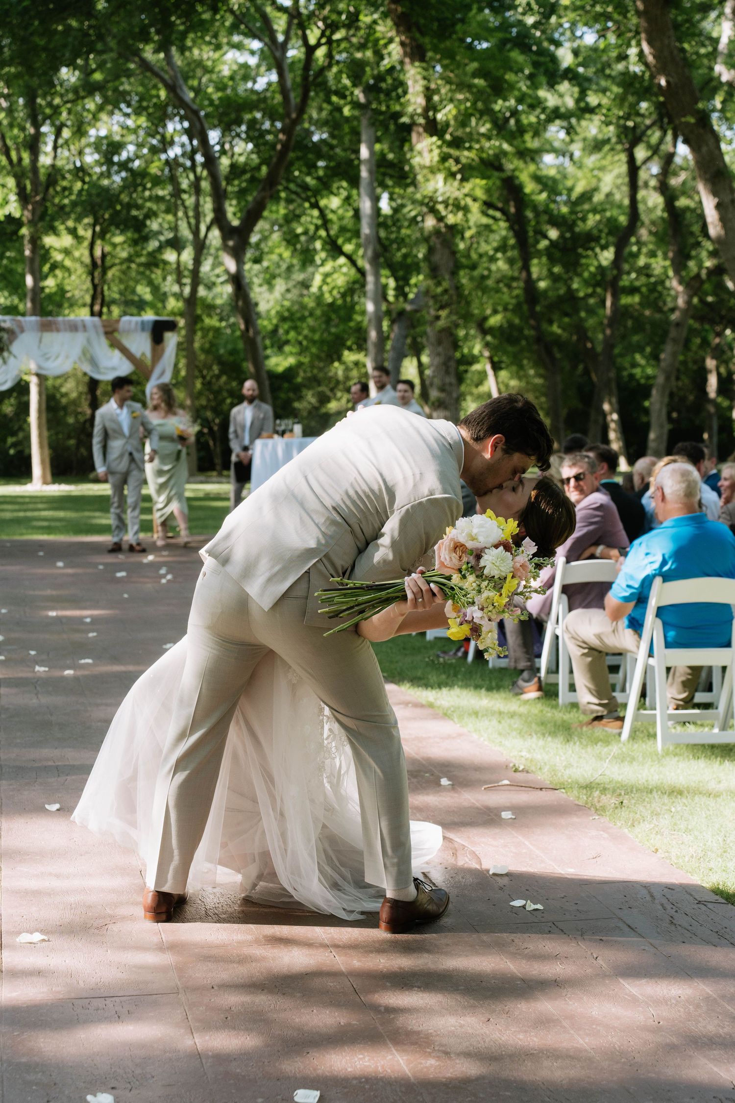 Couple shares romantic dip kiss during outdoor wedding celebration.