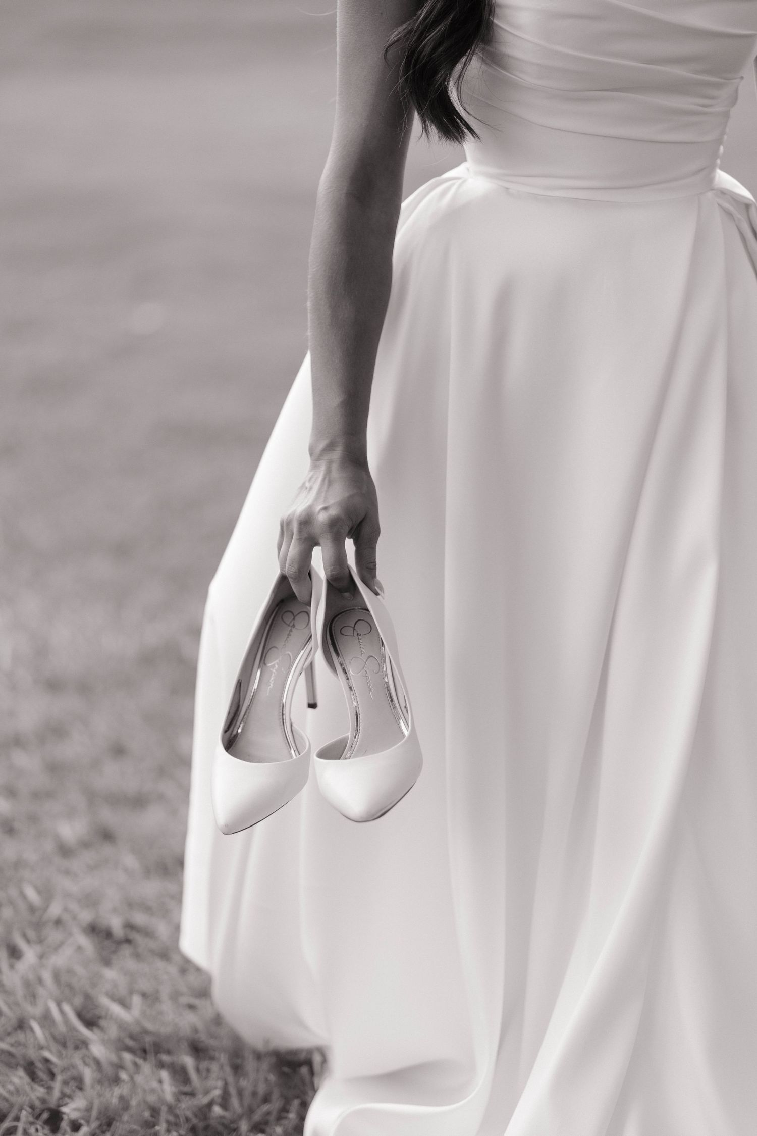 Close-up of bride holding white wedding shoes against her flowing dress.