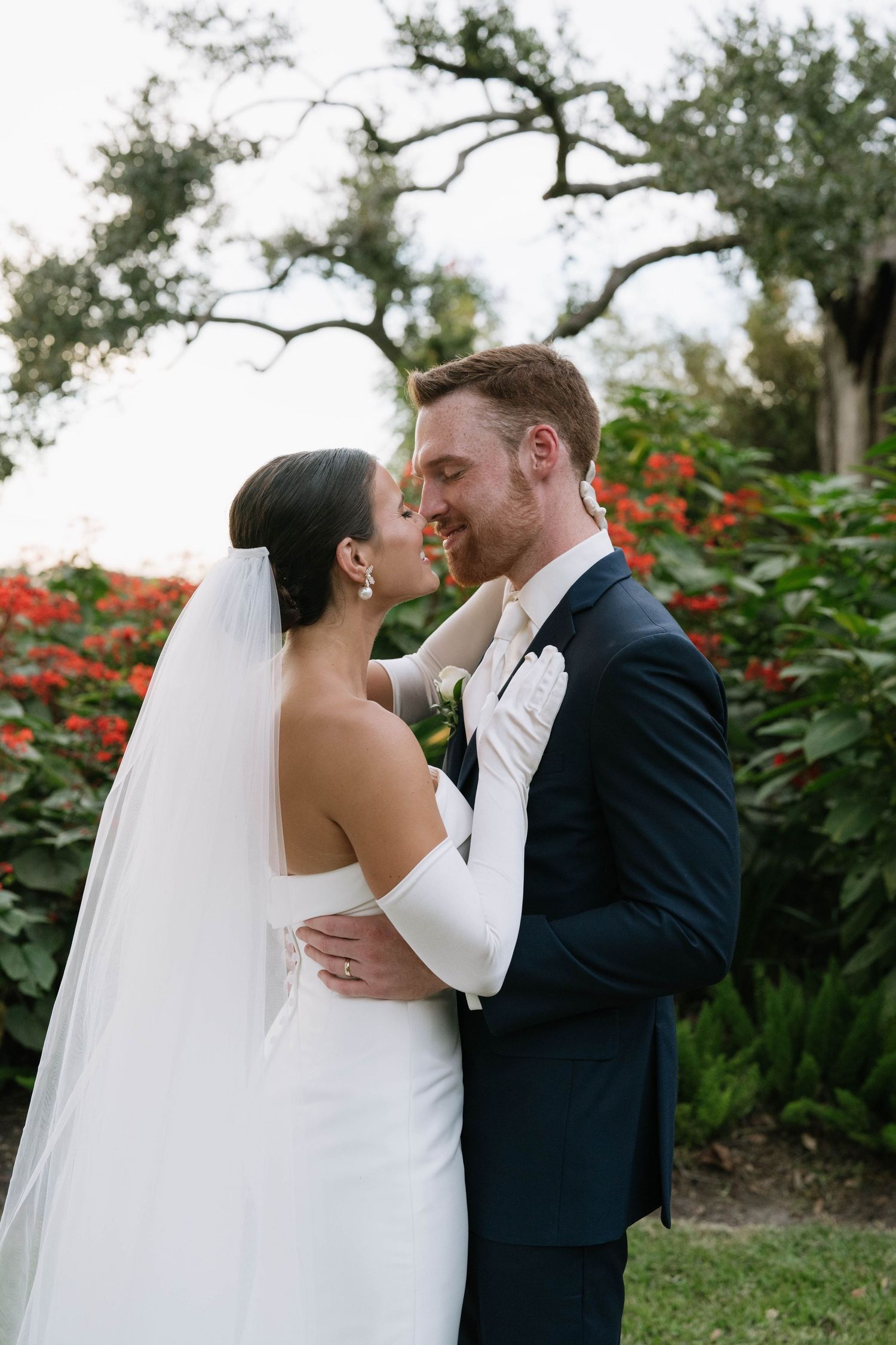 Romantic garden wedding portraits with blooming red flowers in the background.