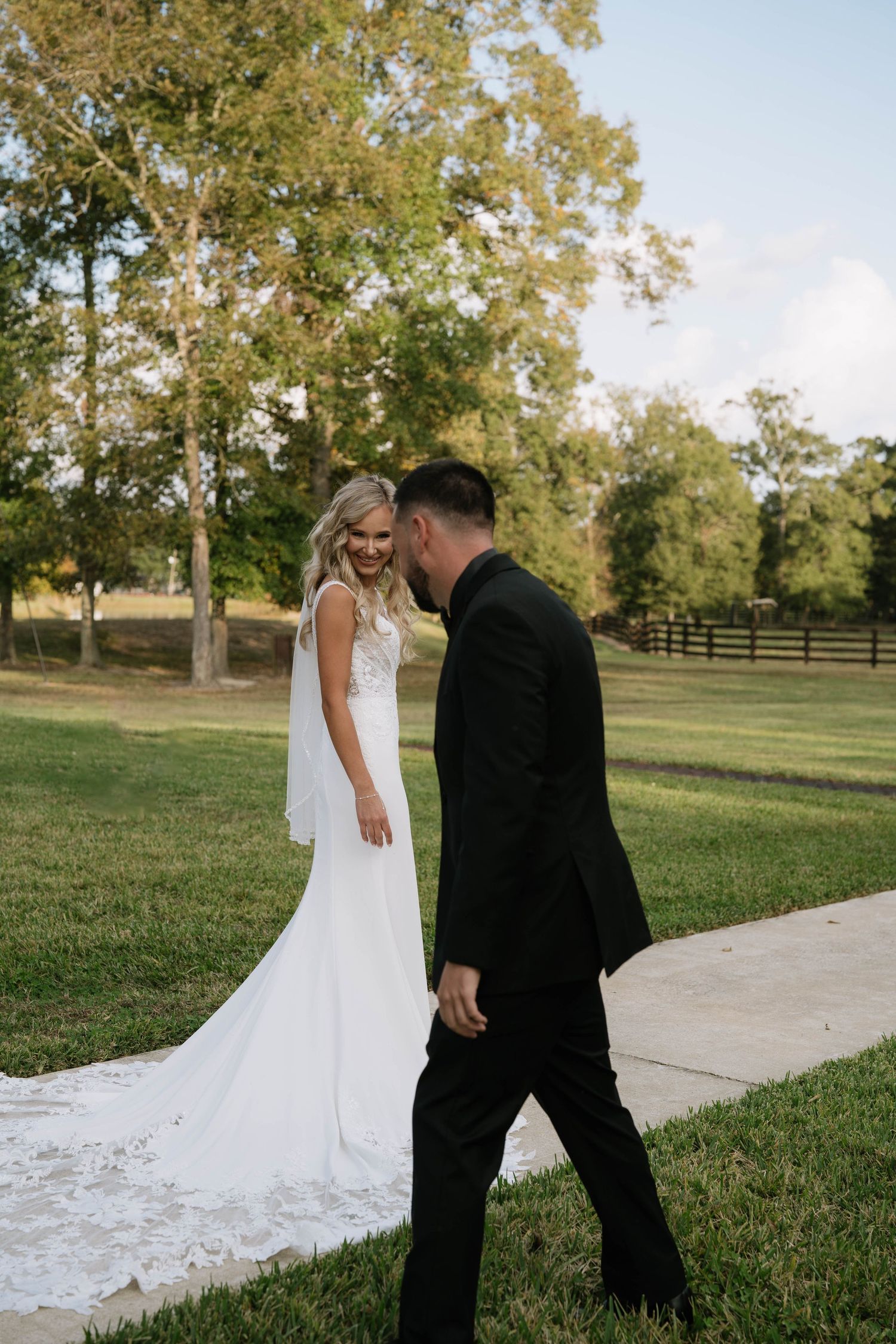 Wedding couple walking together on a paved path in a grassy field.