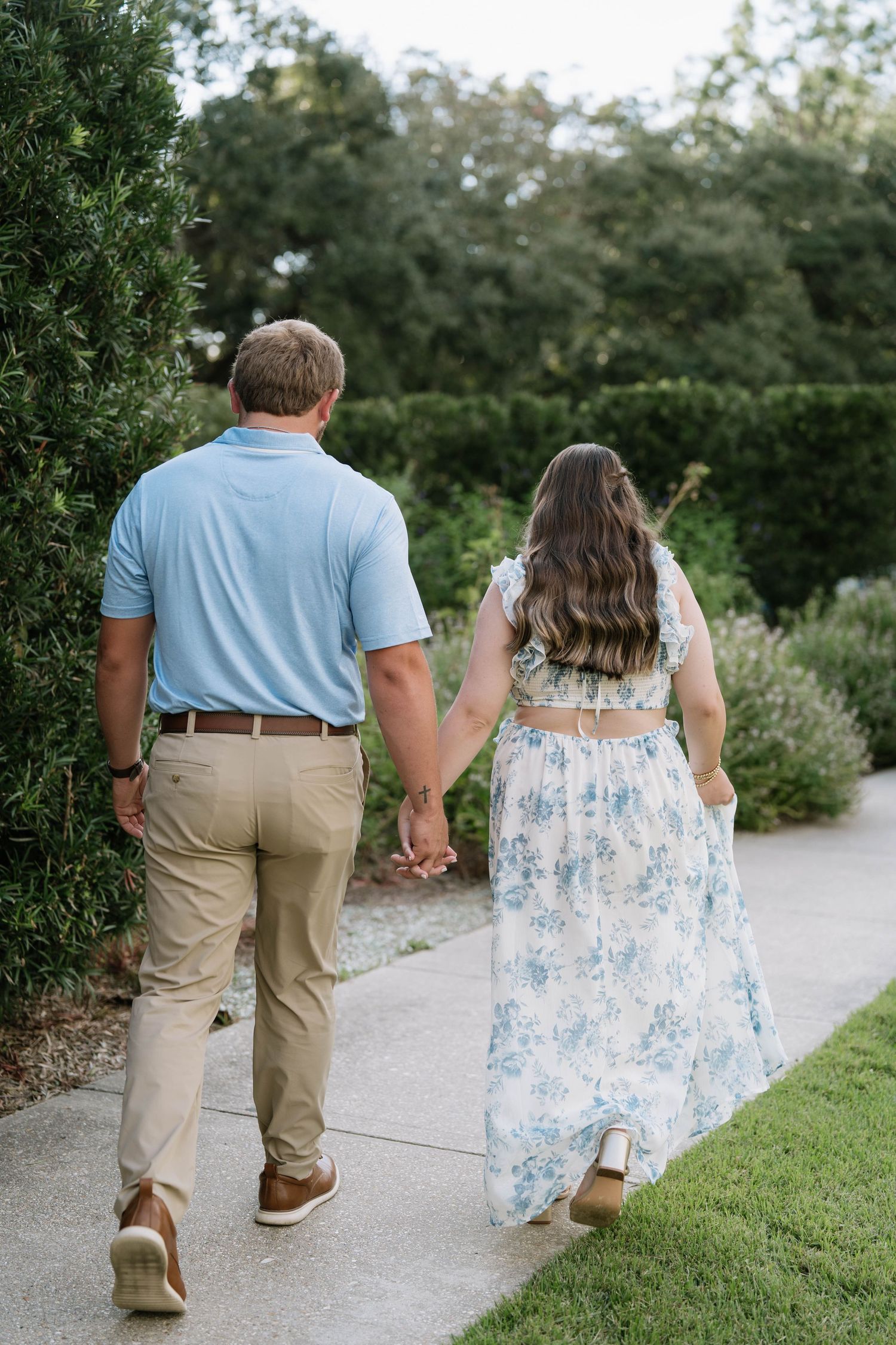 Couple walking hand in hand on outdoor path wearing blue and floral summer outfits.