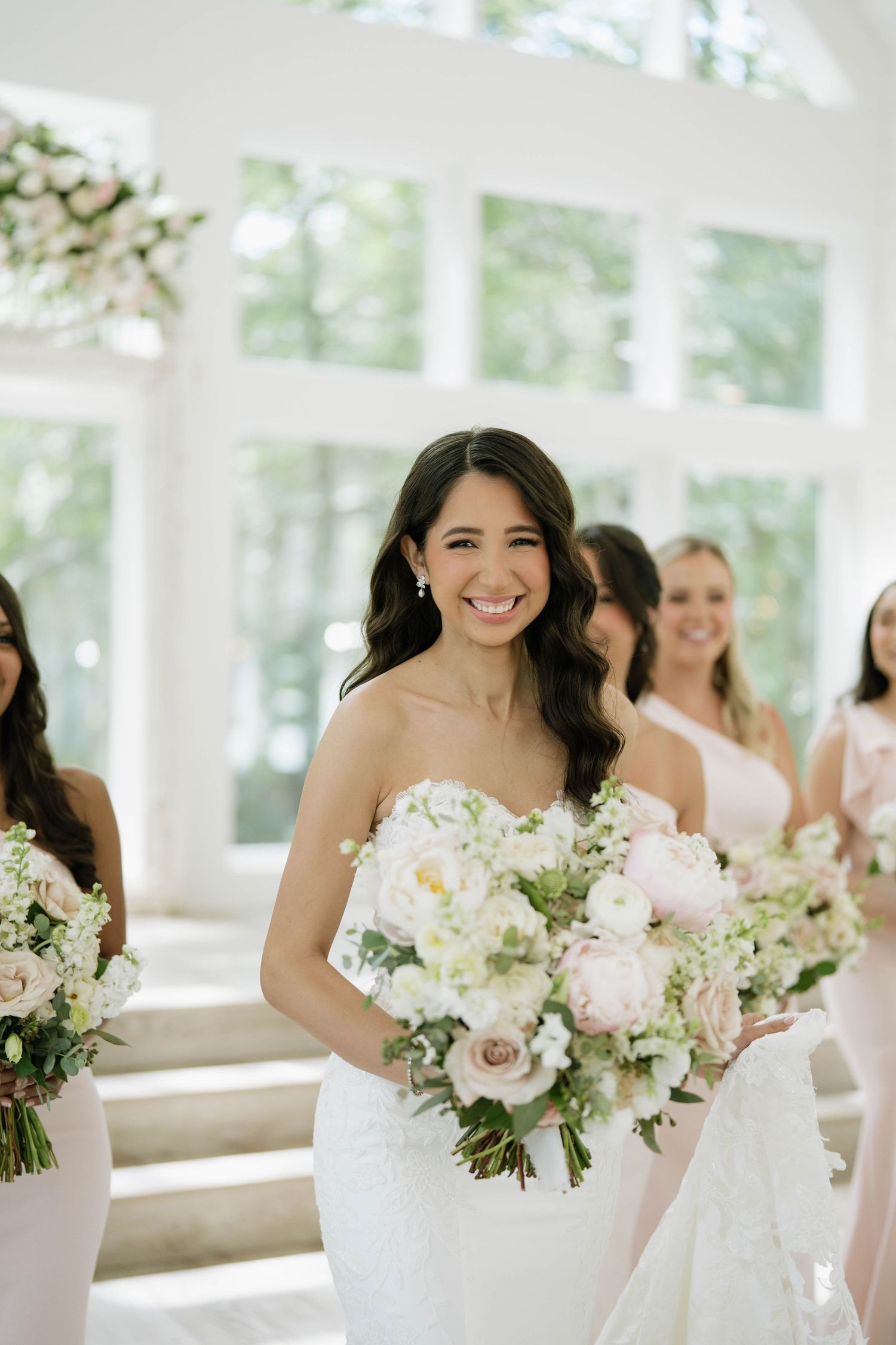 A wedding party in white dresses holding delicate bouquets of white and blush flowers.