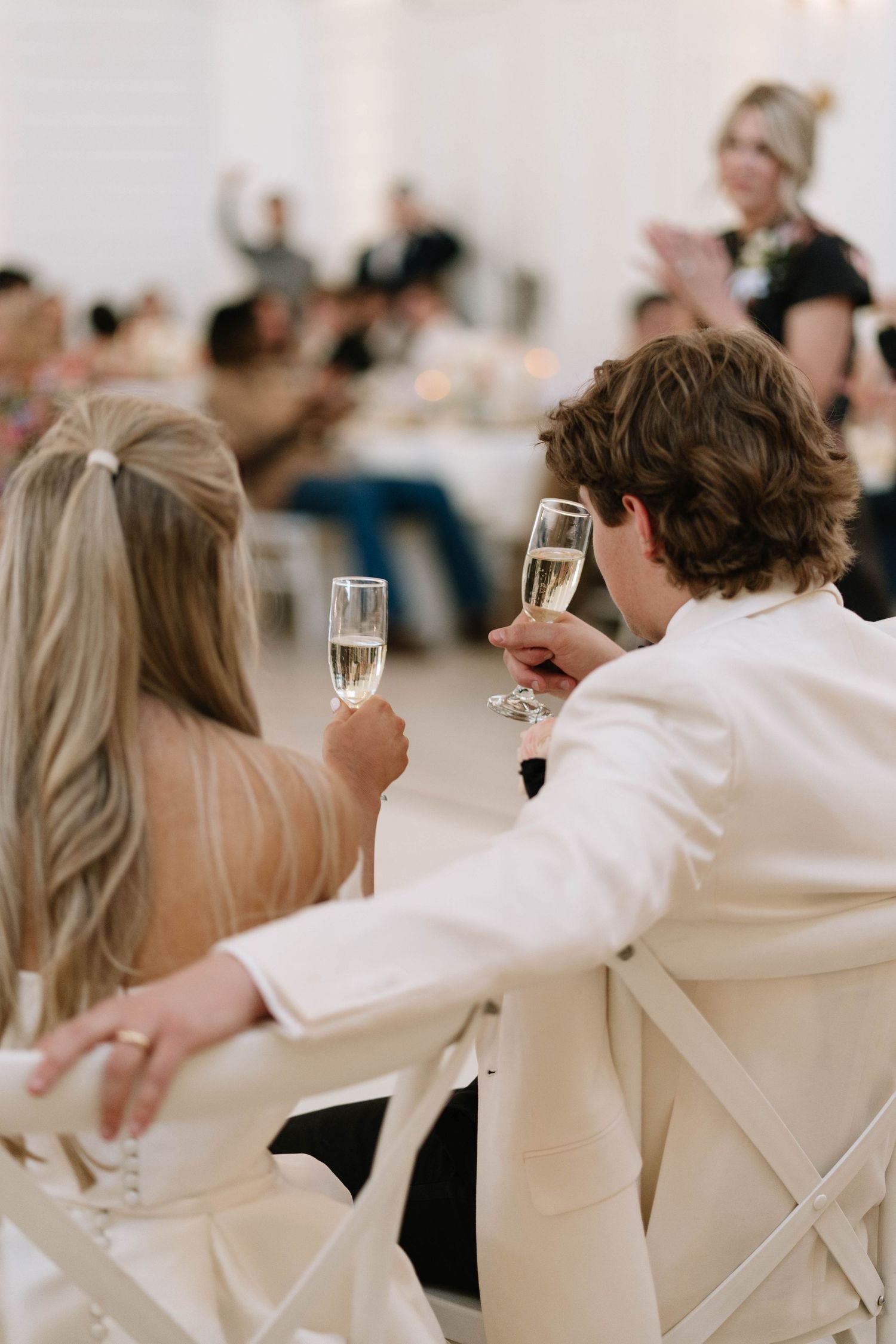 Wedding guests in white attire seated at reception tables during a celebration.