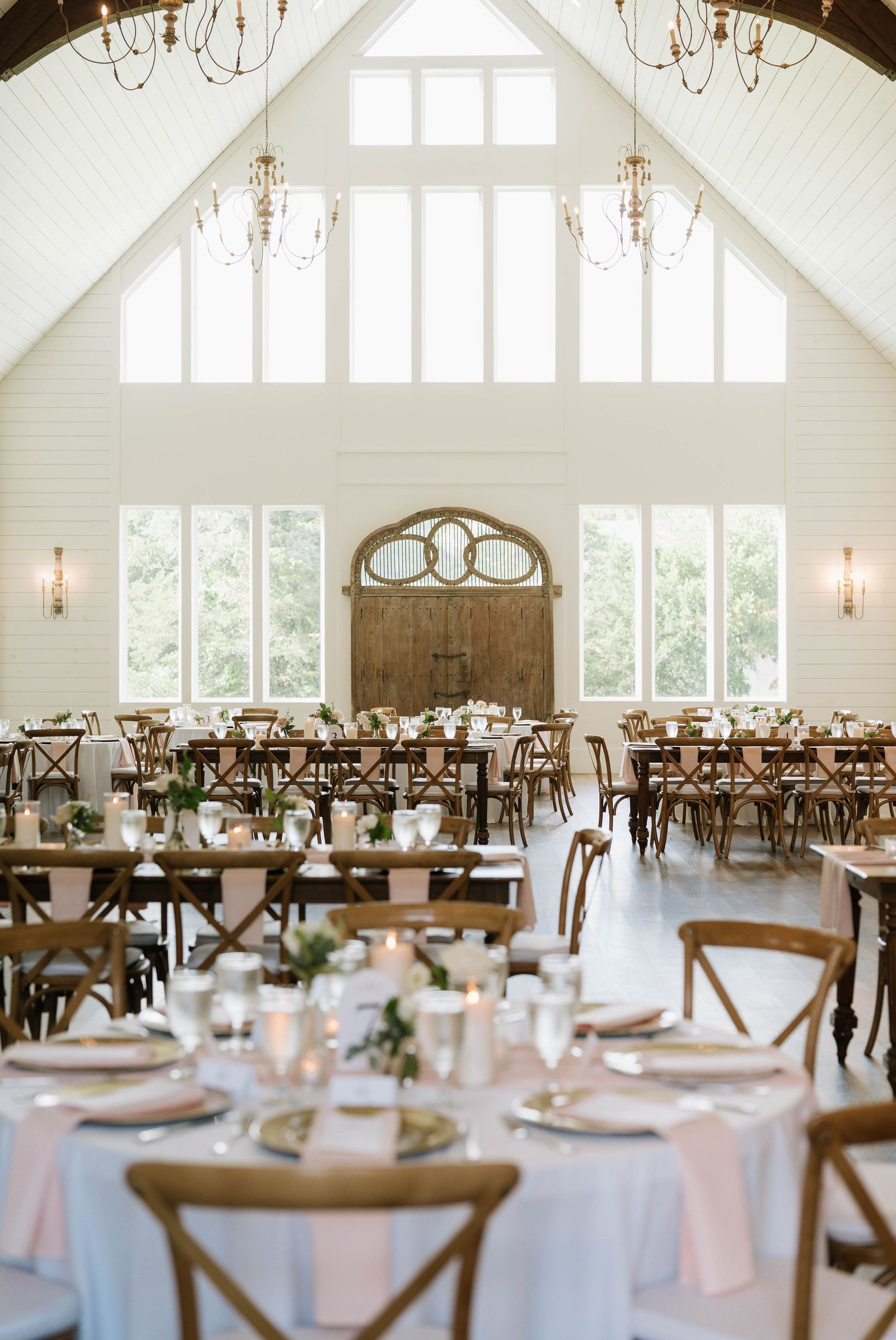 Elegant wedding reception hall with vaulted ceilings and rustic wooden cross-back chairs.