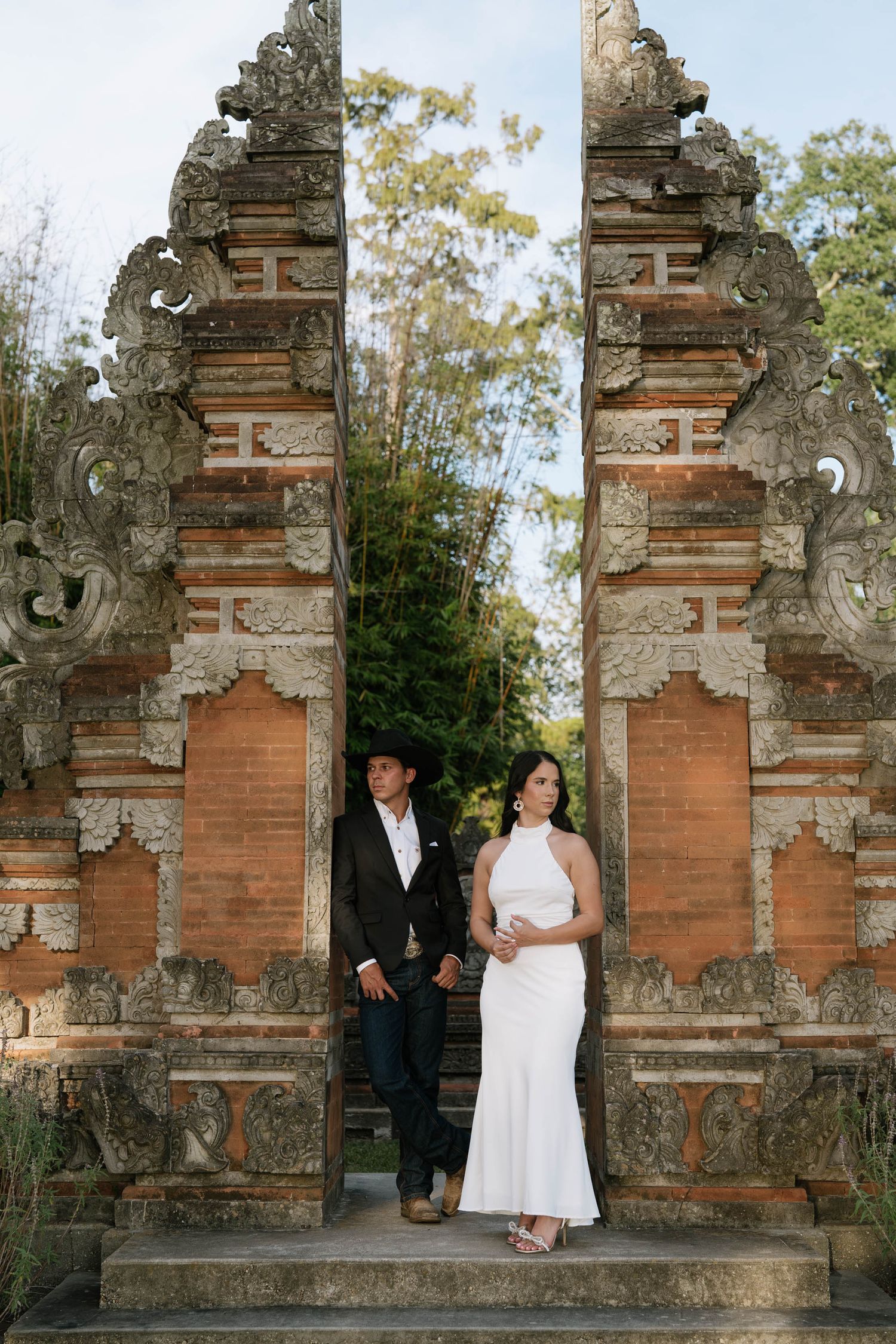 A couple poses between ornate Balinese temple gates in formal attire.
