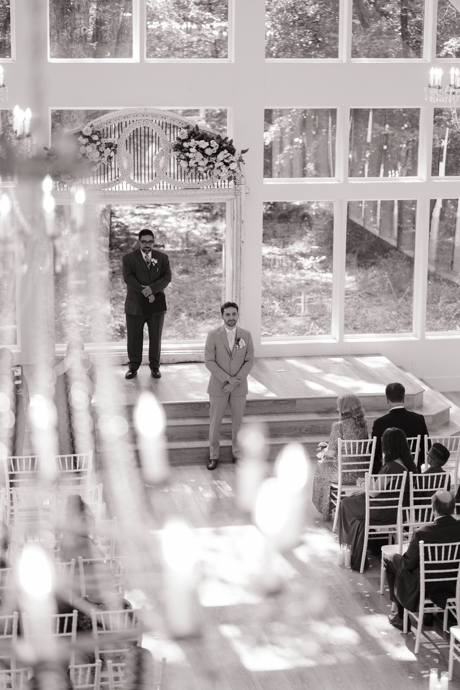 Wedding ceremony setup in a bright glass-walled venue with white chiavari chairs.