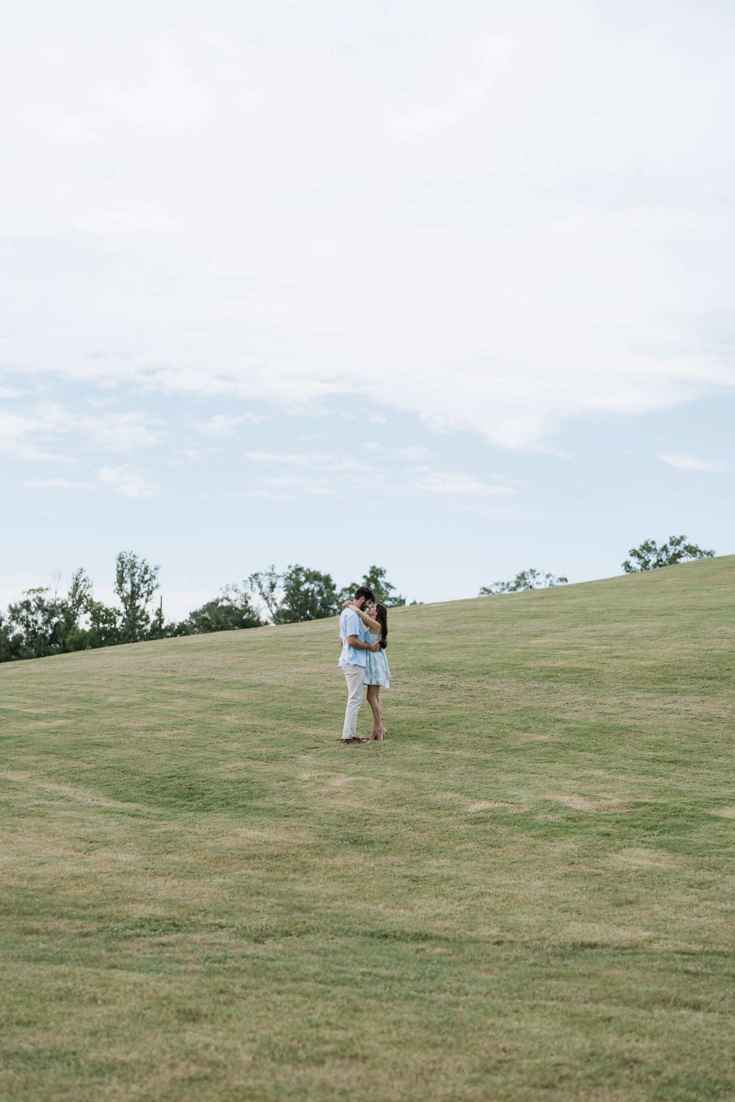 Figures stand on rolling green hillside against cloudy sky.