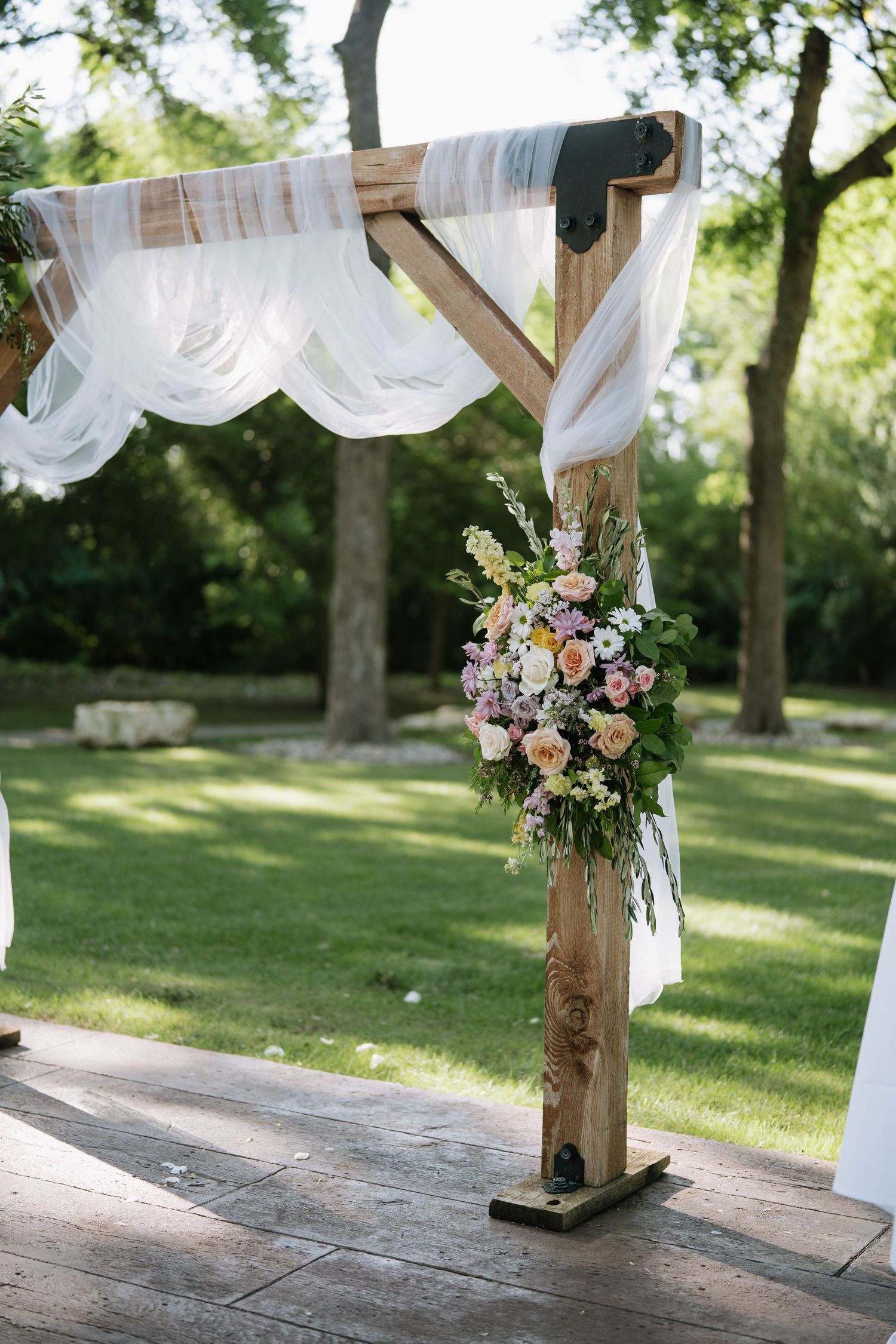 Rustic wooden wedding arch decorated with white fabric and pink floral arrangements.
