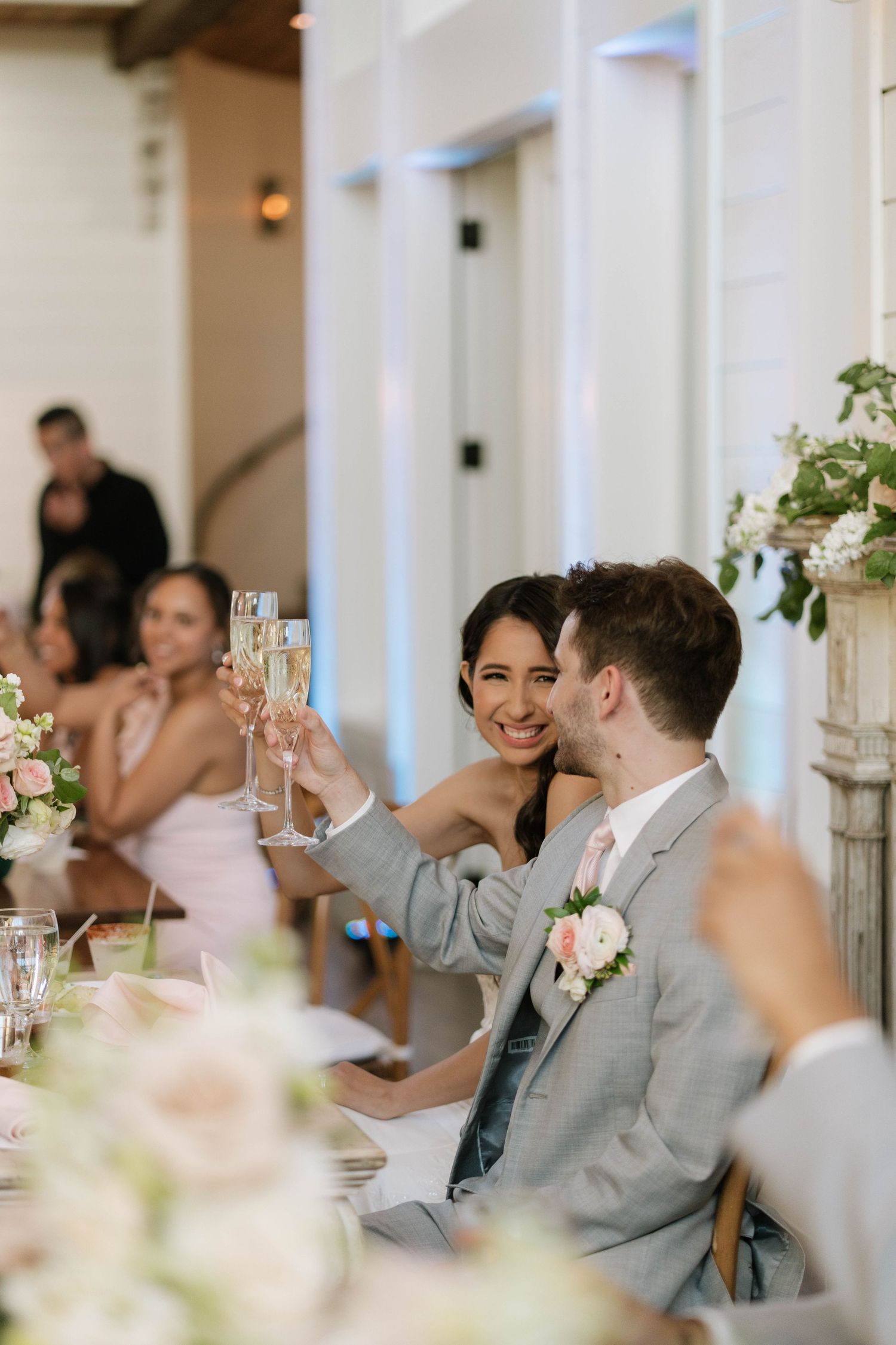 Wedding guests in formal attire raising glasses for a toast during reception.