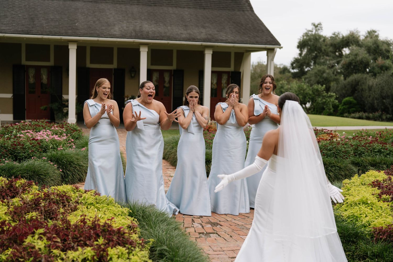 Bridesmaids in pale blue dresses react emotionally to first look at bride.