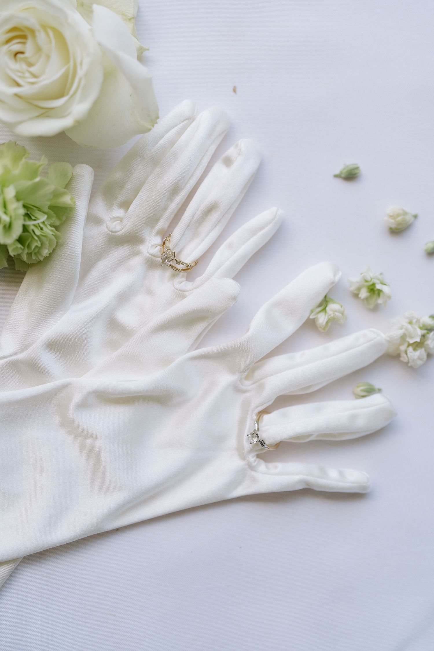 White satin gloves with delicate floral accents and pearls on a light background.